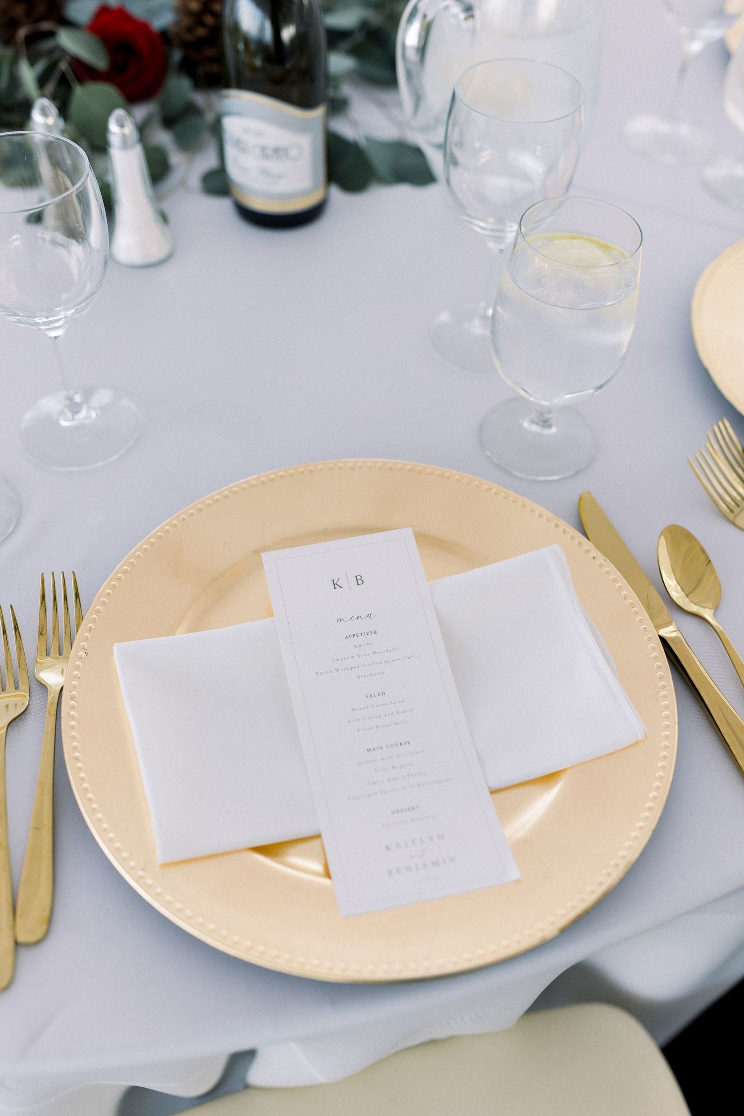Wedding place setting with gold charger plate, menu card, and gold cutlery.