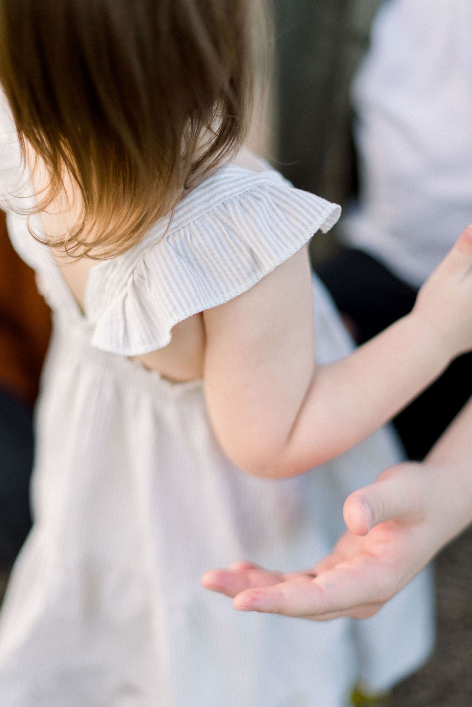 Close-up of white ruffled dress detail and reaching hand.