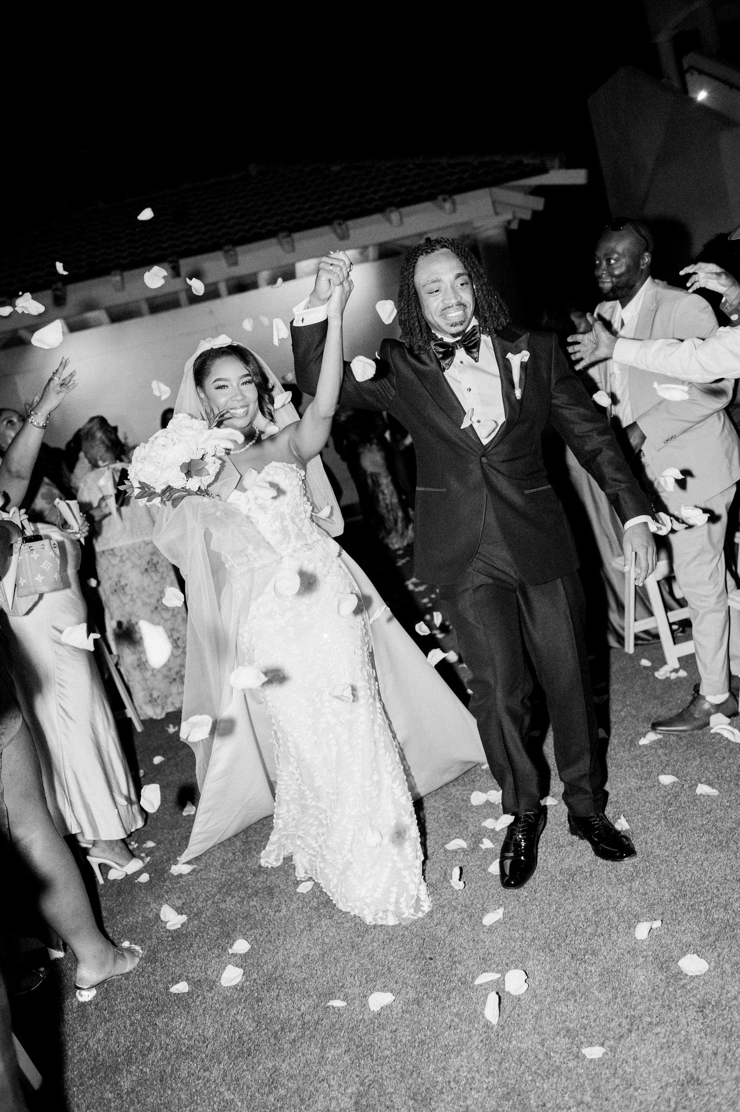 Black and white photo of wedding couple dancing and celebrating with guests throwing flower petals.