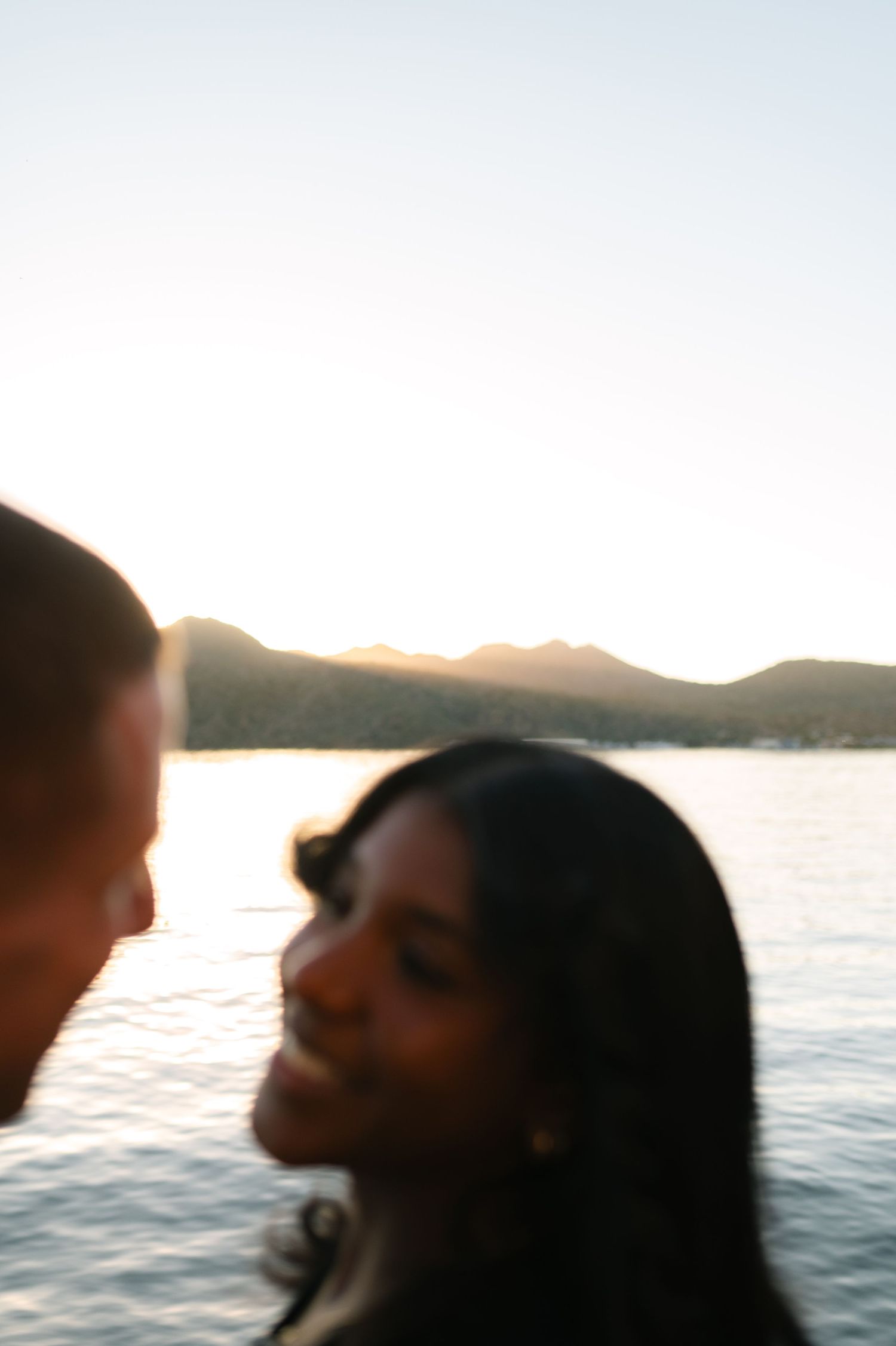 Silhouettes against a sunset over a lake with mountains in the background creating a romantic atmosphere.