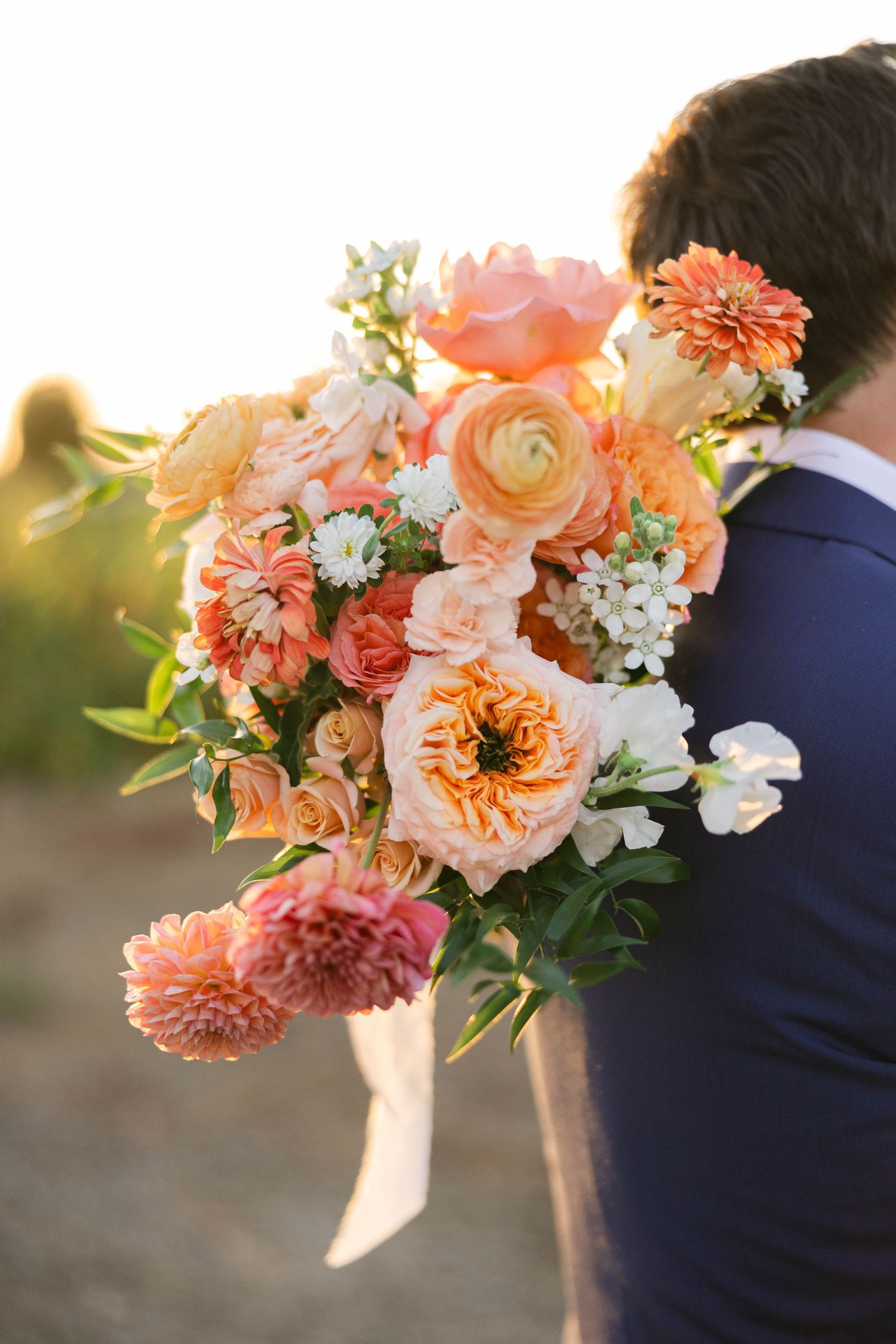 Peach and coral wedding bouquet glows in golden sunlight.