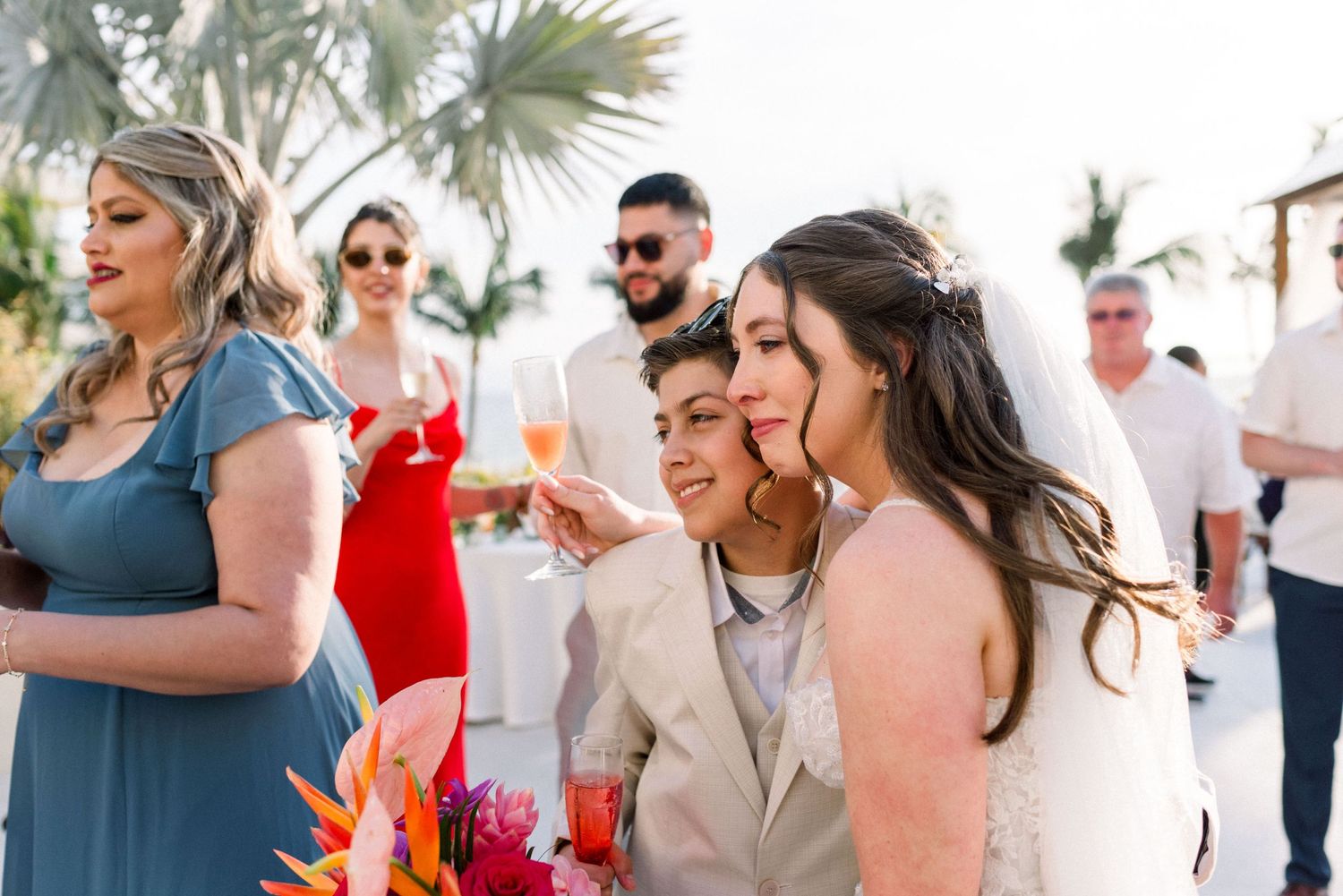 Wedding guests gather outdoors with tropical palm trees and festive drinks at a destination celebration.