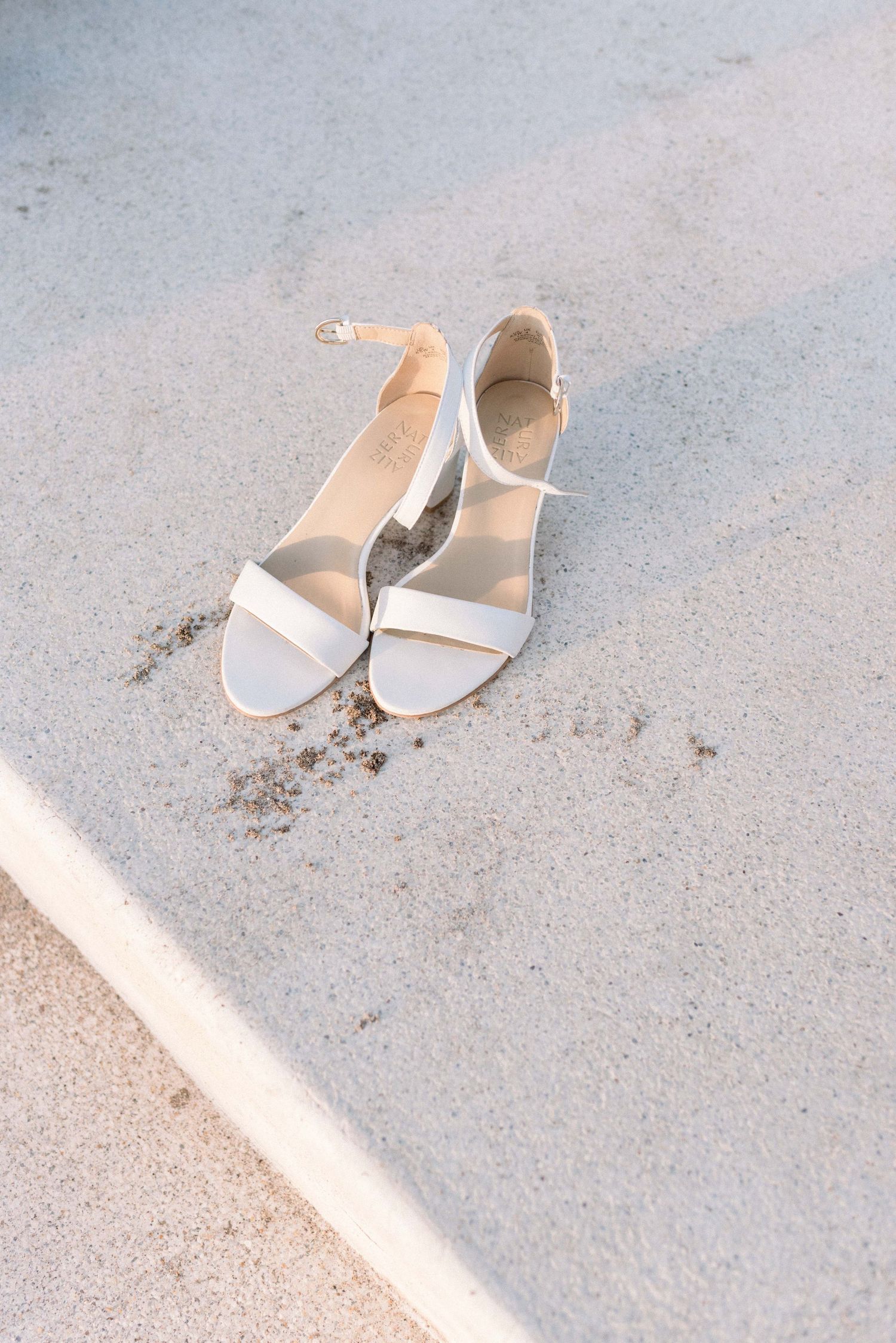 White strappy sandals on concrete in natural sunlight.