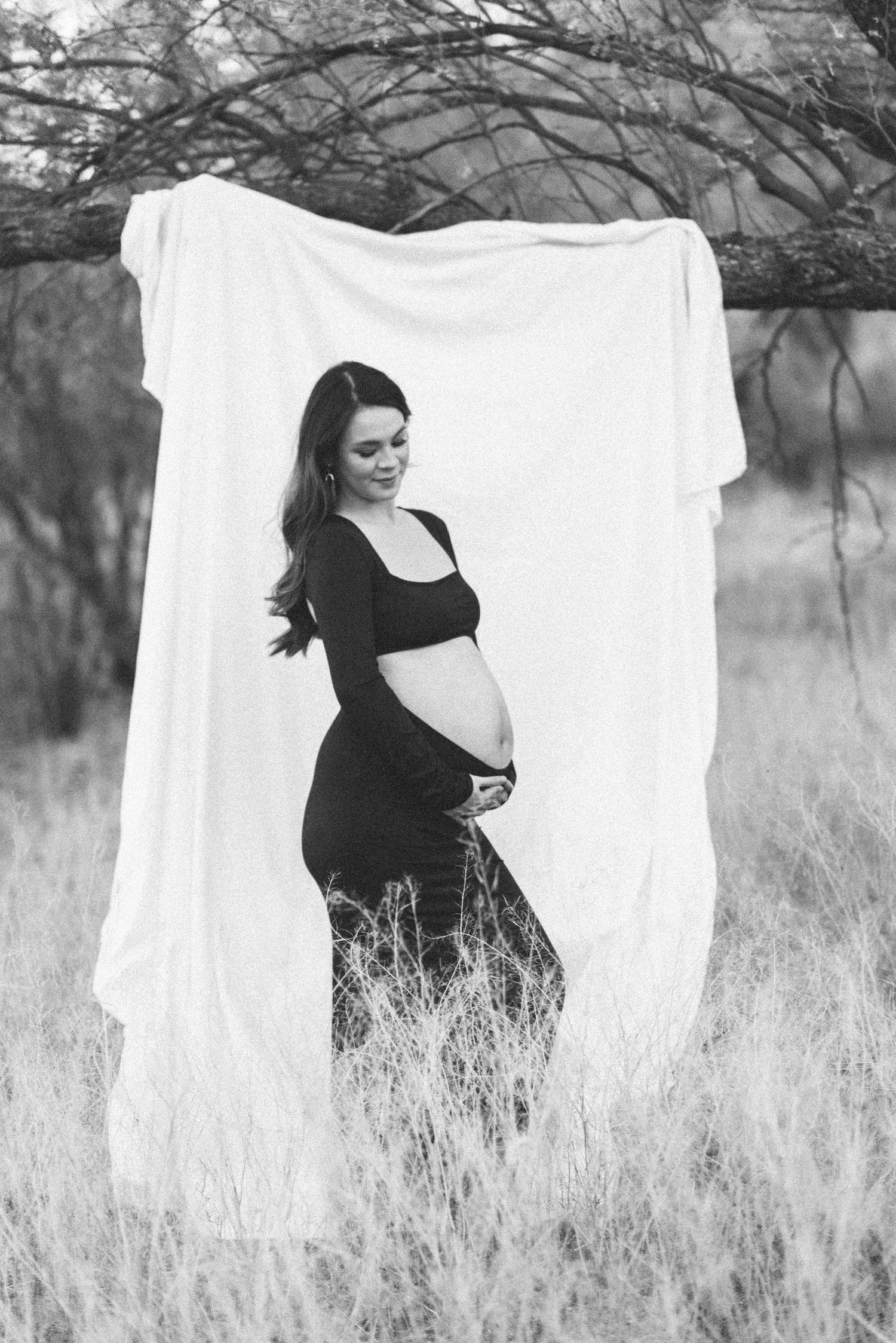 Black and white maternity portrait with white backdrop in natural setting showing pregnancy silhouette.