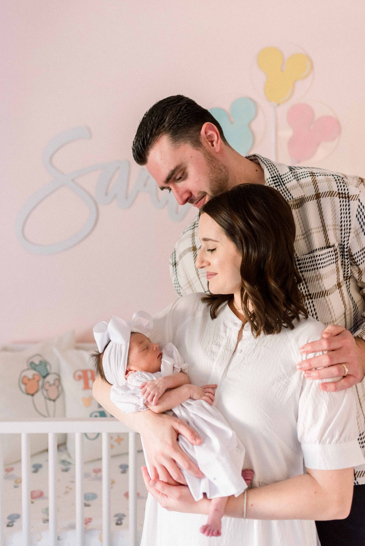 New parents sharing tender moment with newborn in Disney-themed nursery.