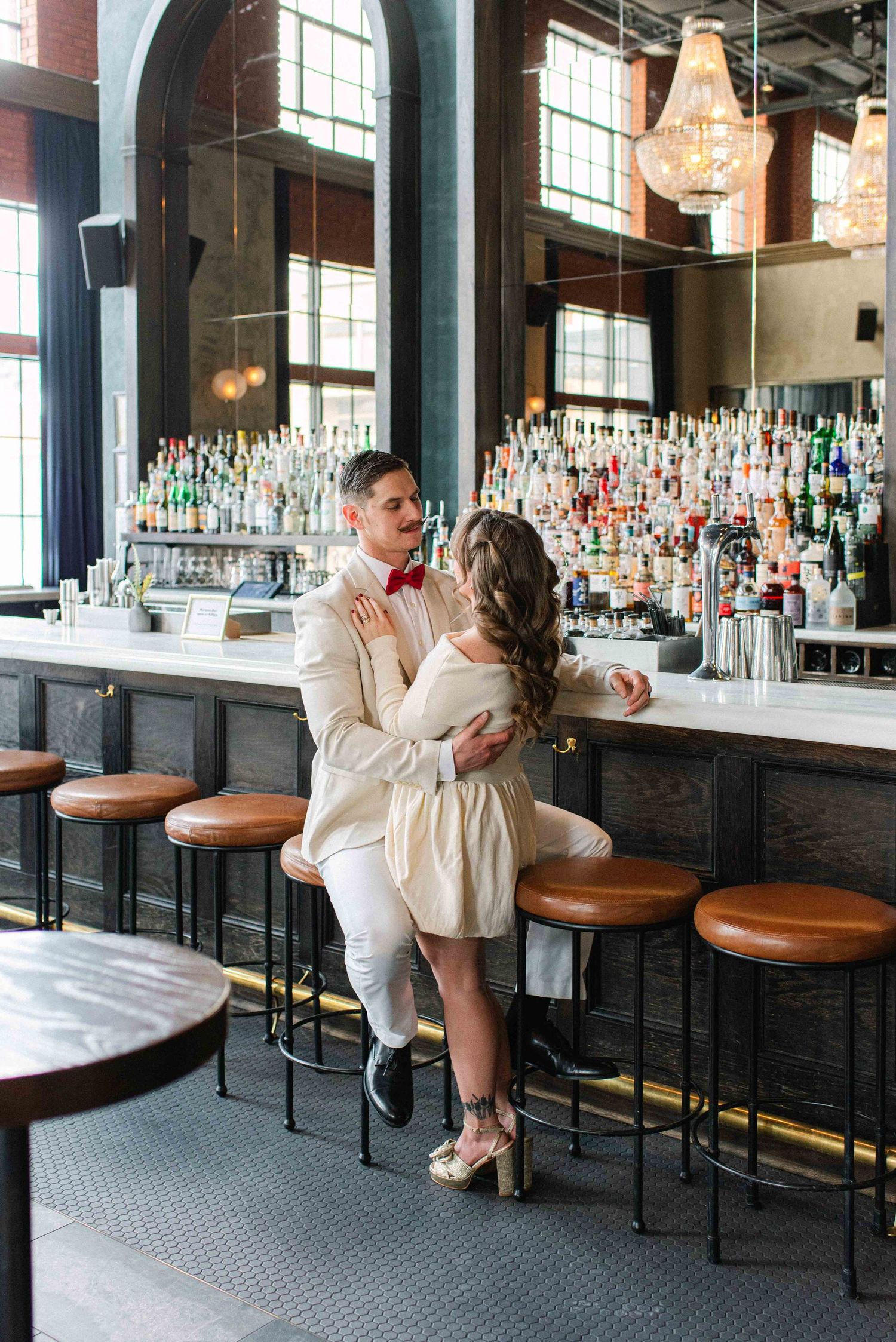 A romantic moment at an elegant bar with arched windows and leather bar stools.