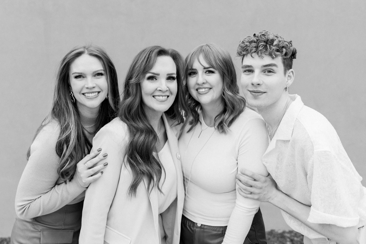 Group portrait in neutral tones against grey background showing coordinated casual outfits.