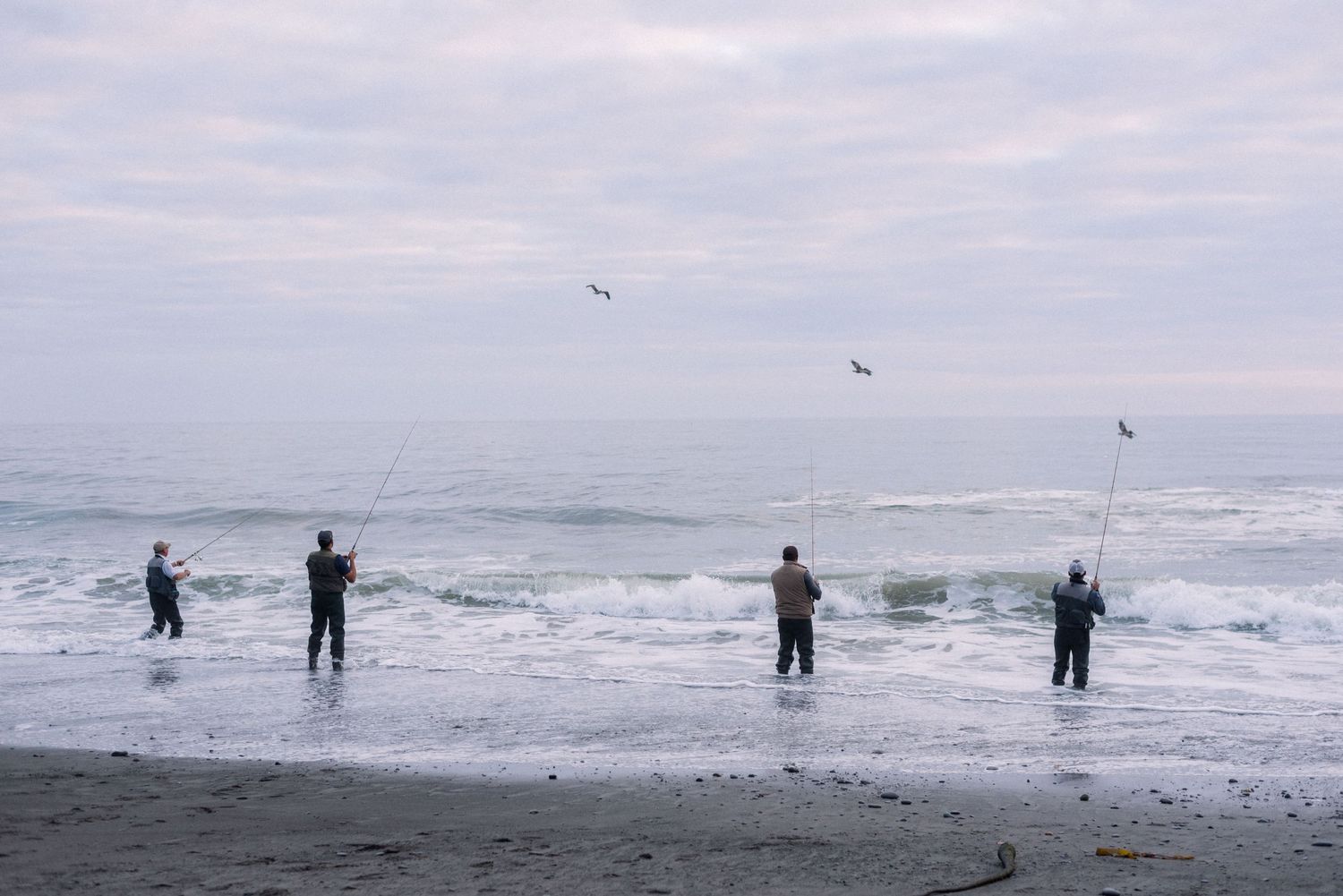 People fly kites on a moody beach with waves crashing in the background.