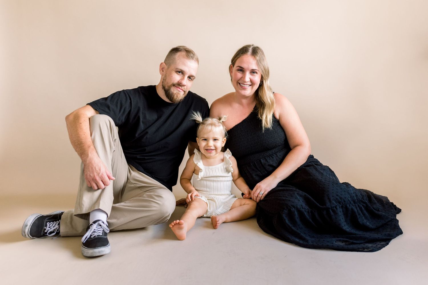 Family of three posing together for portrait on neutral studio background.