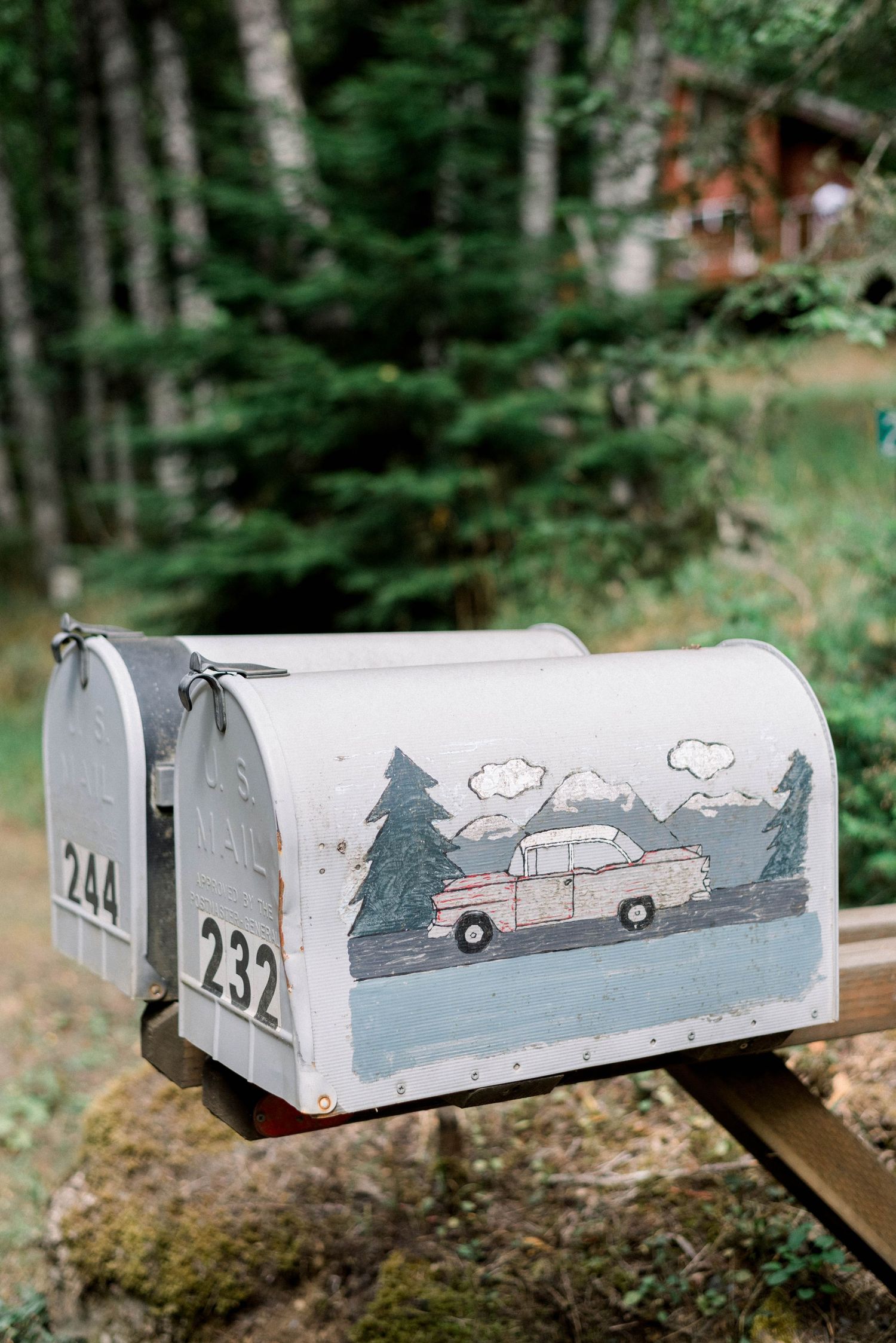 White mailbox with hand-painted scene of vintage truck and trees in forest setting.