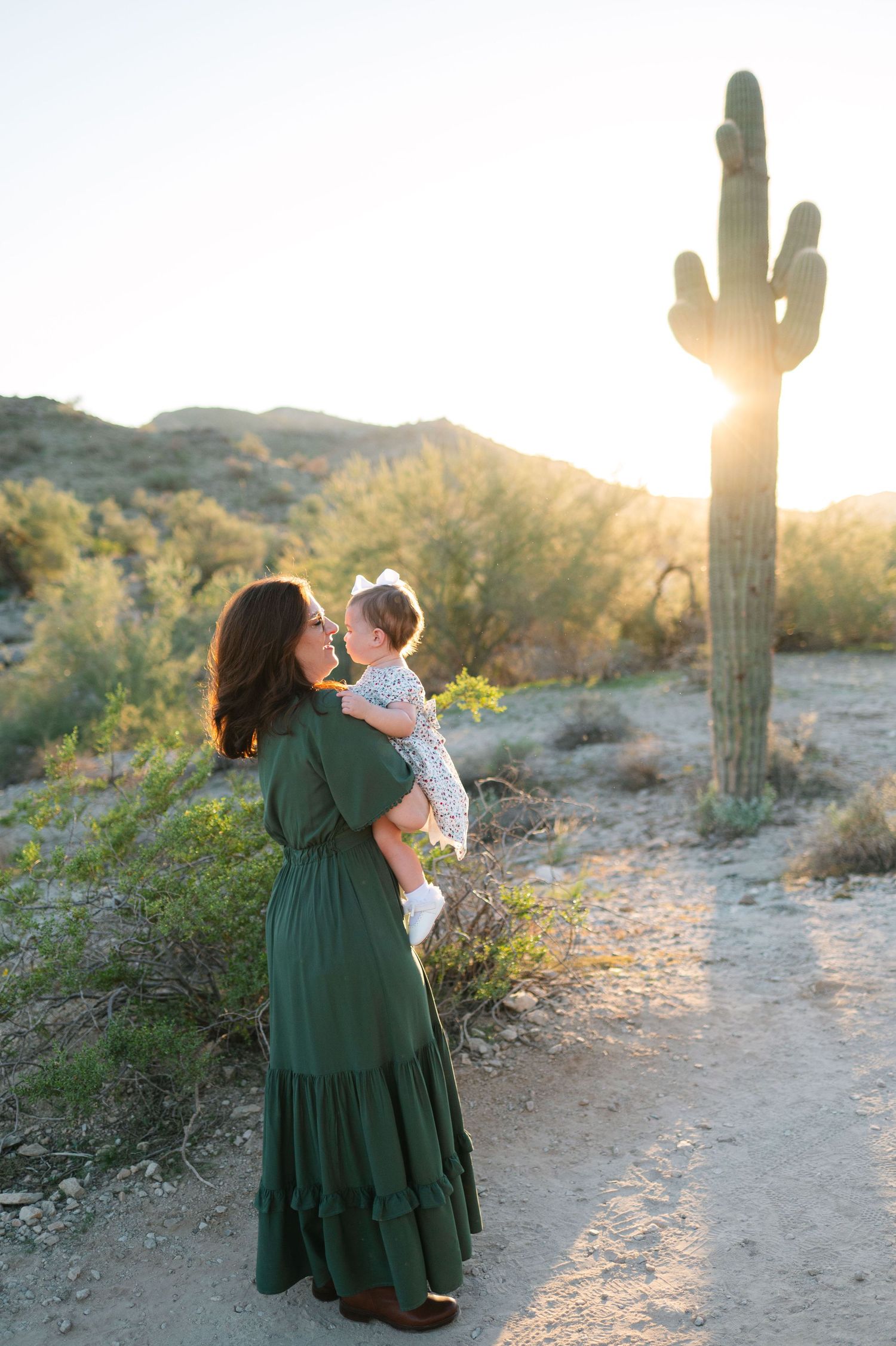 A tender family moment captured against a desert landscape with saguaro cacti at golden hour.