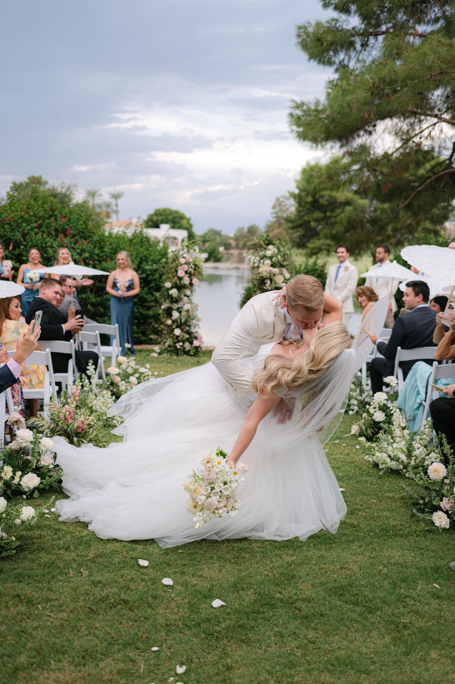Wedding party members in flowing white dresses pose together on green grass.