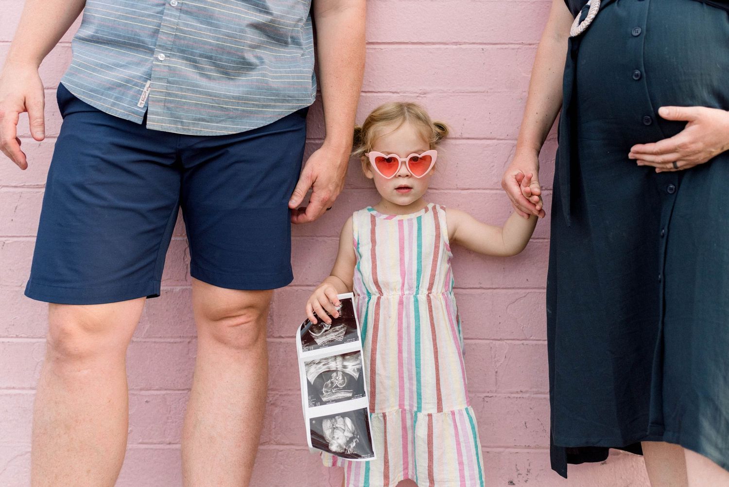 People standing together holding ultrasound photos against a pink wall.
