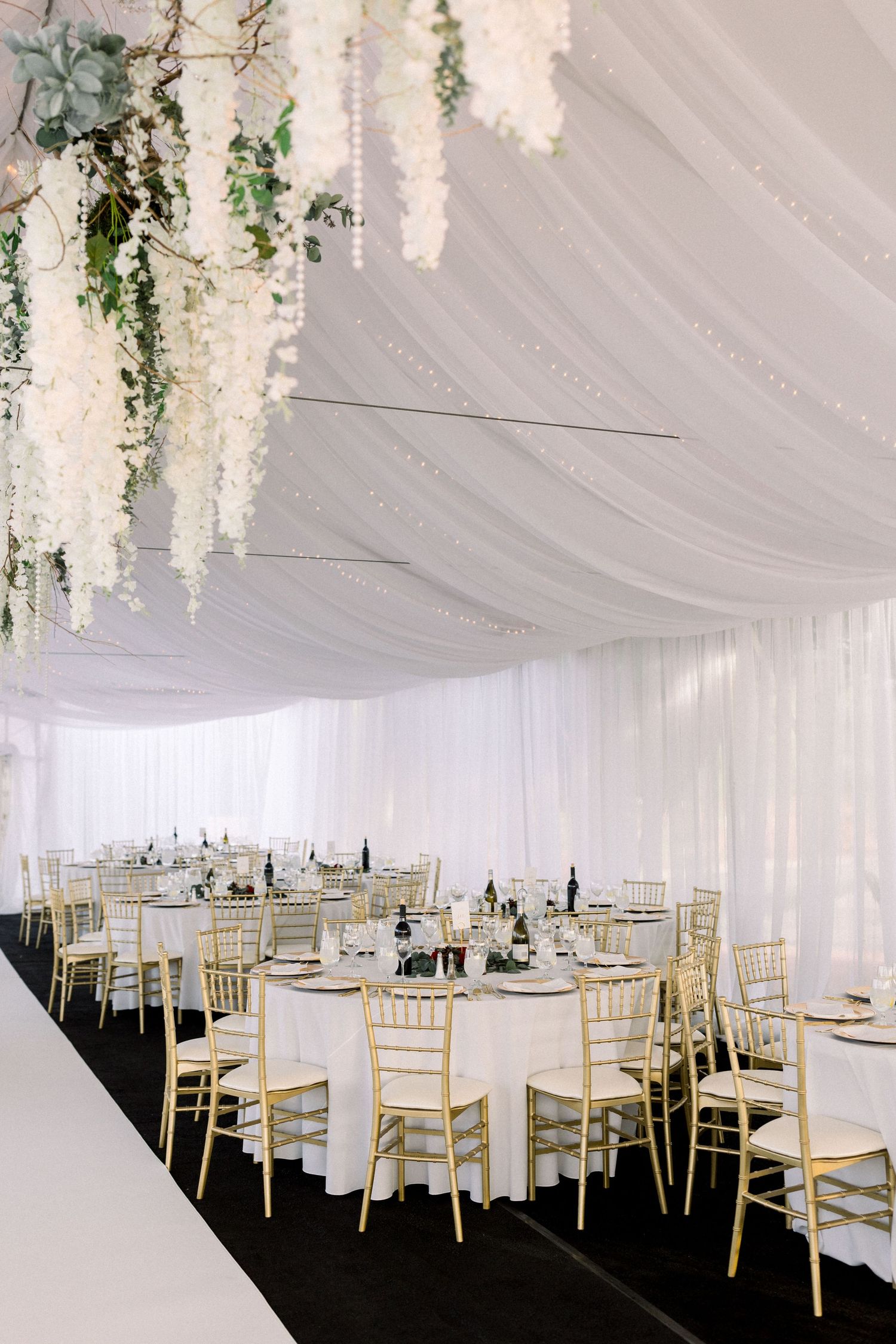 Wedding reception setup with round tables and cascading white floral ceiling installations.