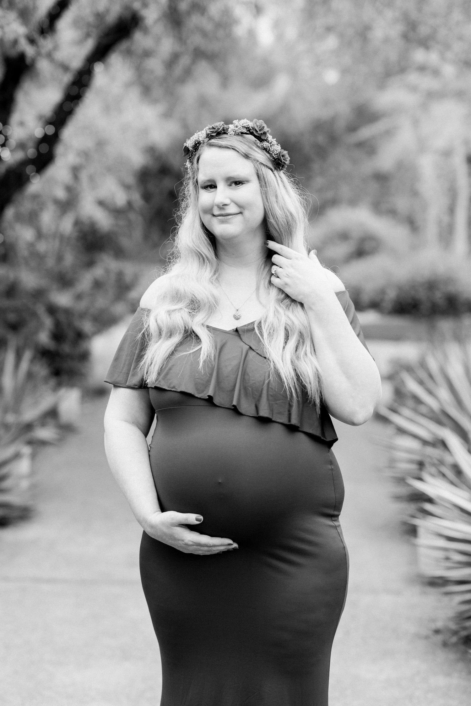Black and white maternity portrait in ruffled dress on garden path with desert landscaping.