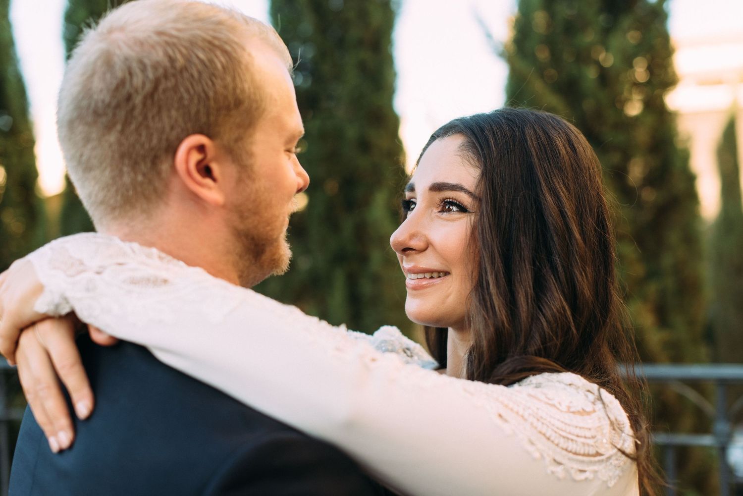 Intimate moment between newlyweds with cypress trees in soft focus background.
