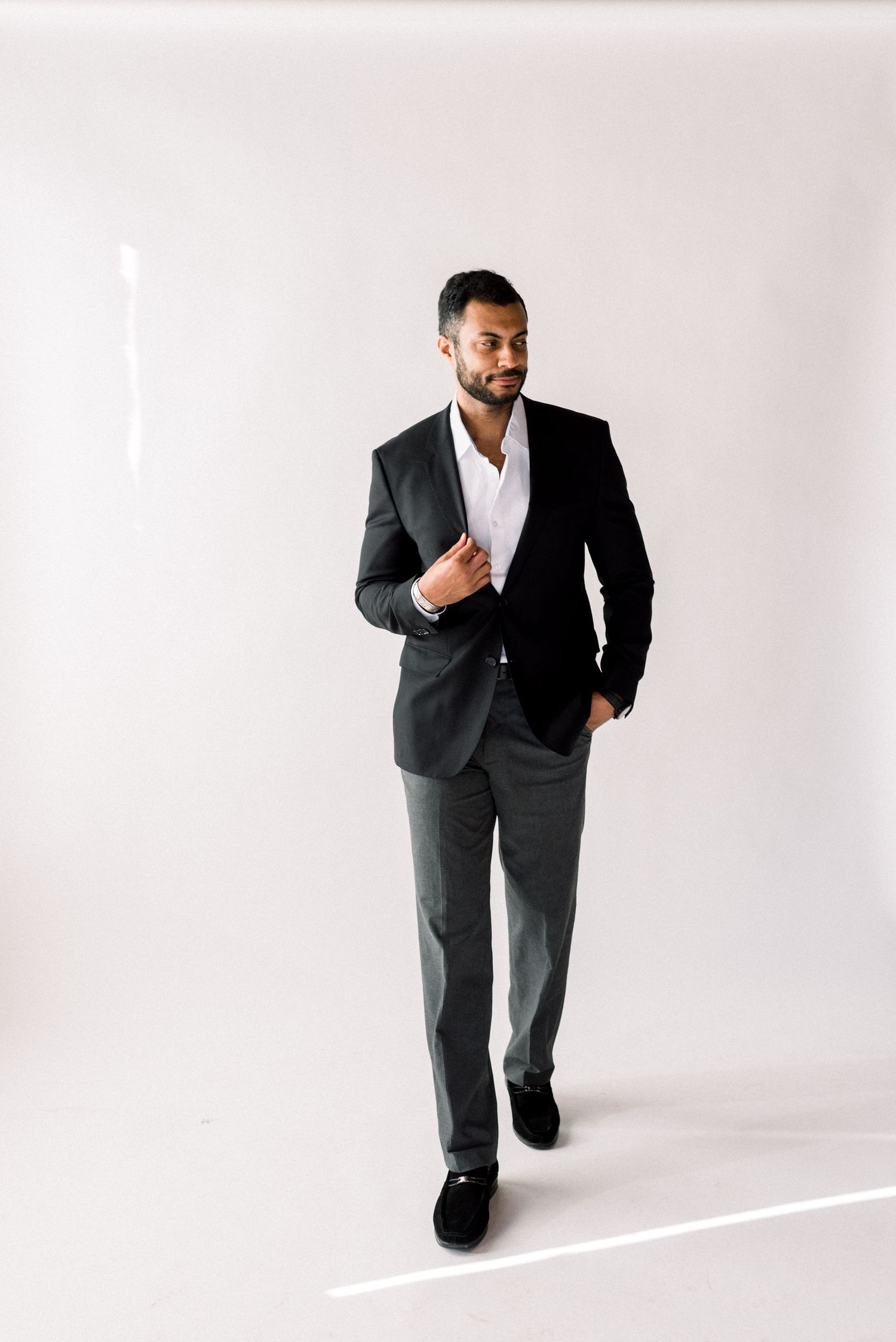 Stylish groom in charcoal suit walking confidently against white backdrop.