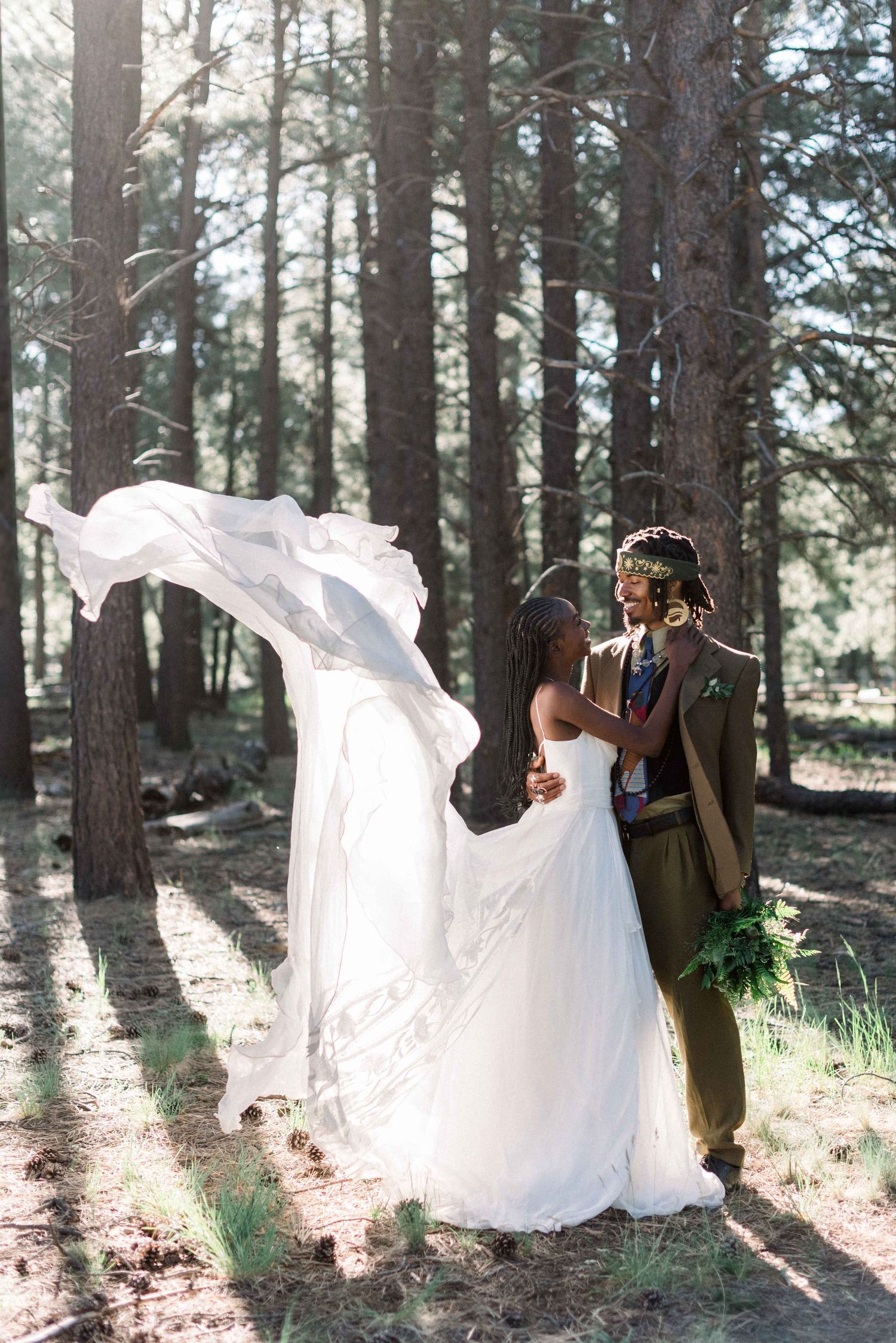 Dramatic wedding photo in a pine forest with flowing white dress.
