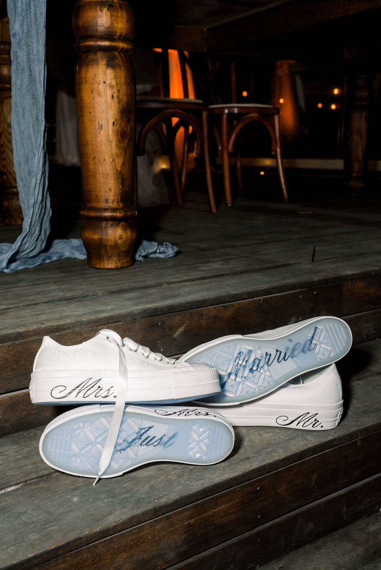 White wedding sneakers with Mrs written in blue script on the soles displayed on wooden flooring.