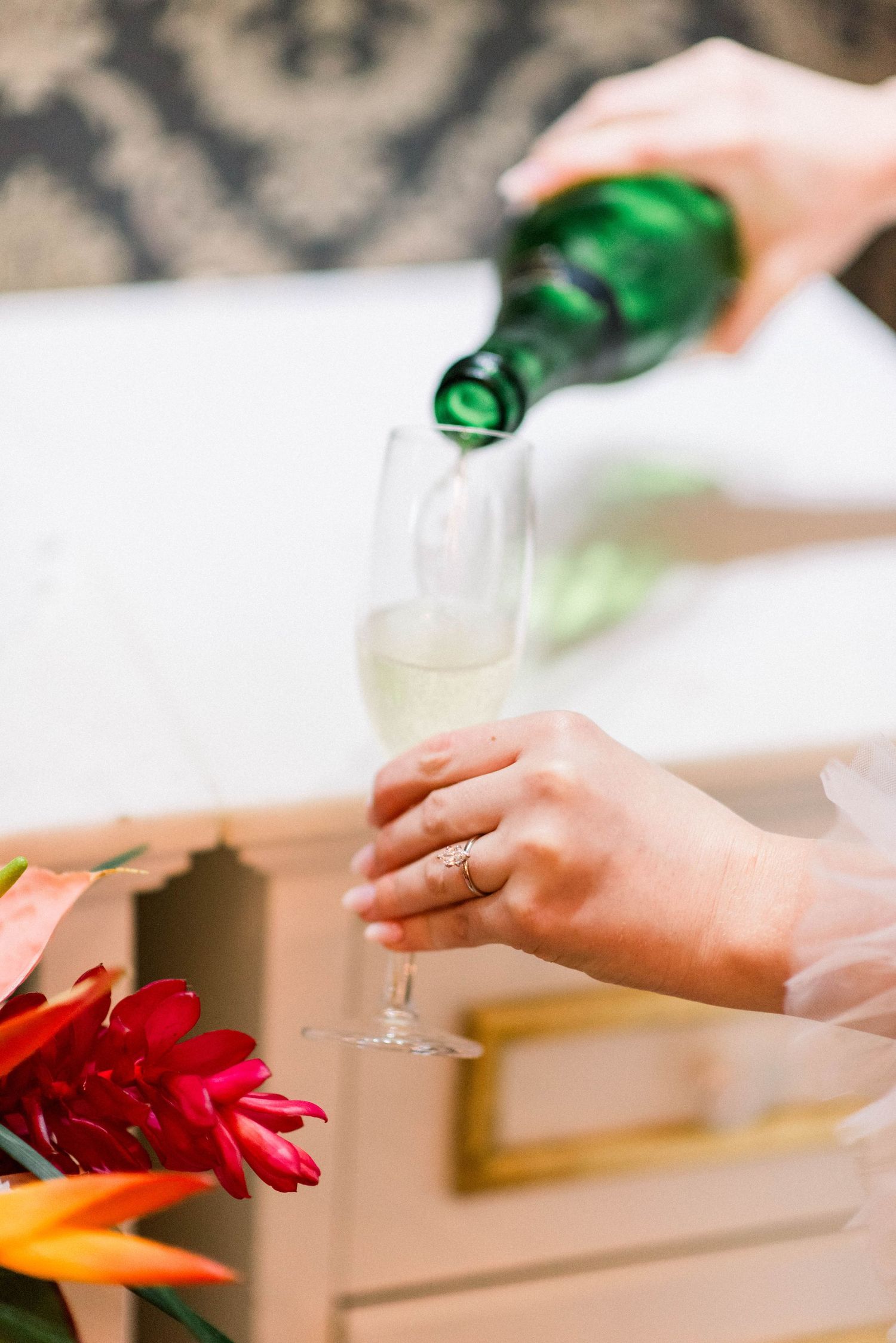 Pouring champagne into a glass with tropical flowers in foreground.