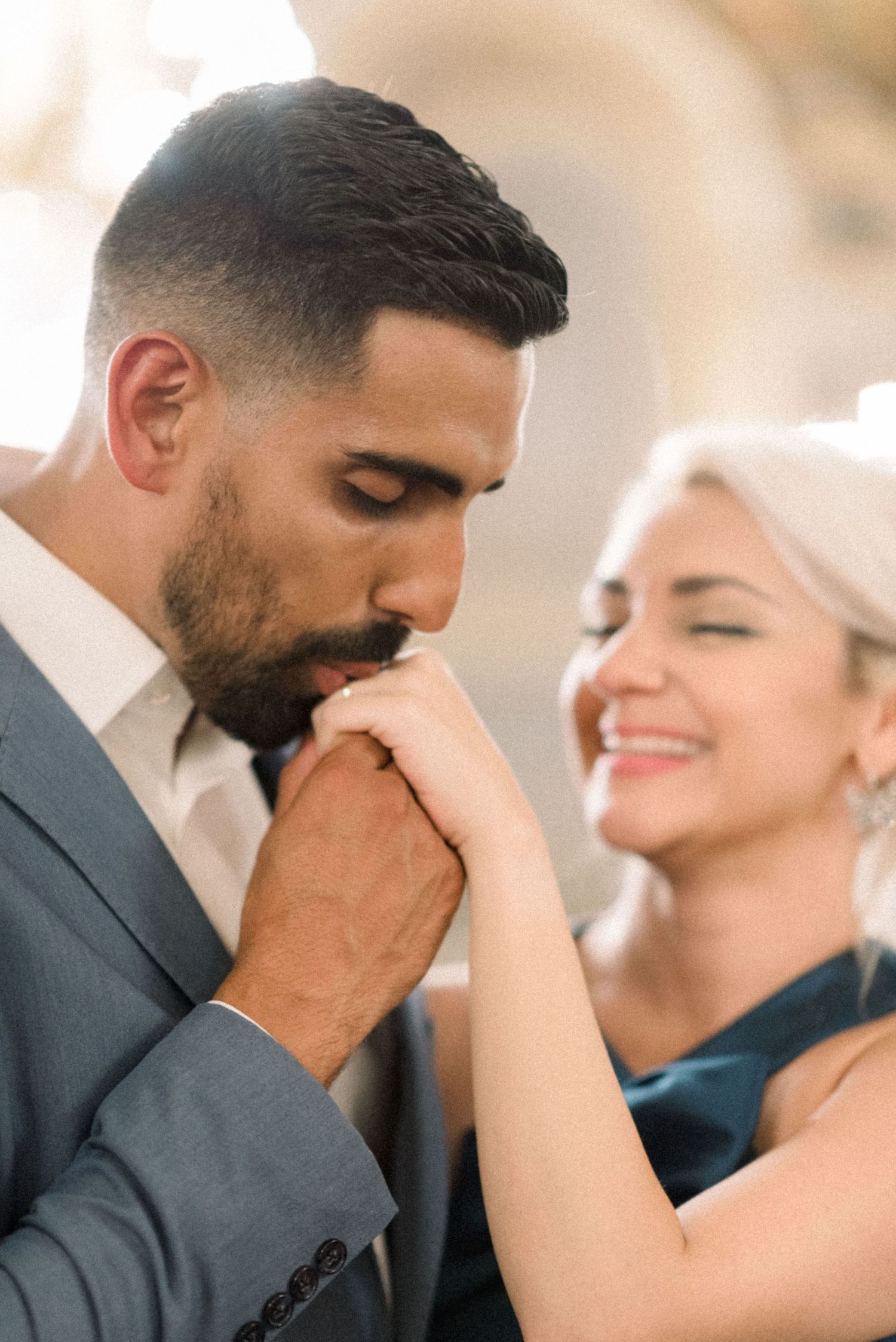 A tender moment captured as a groom kisses his partner's hand in elegant formal attire.