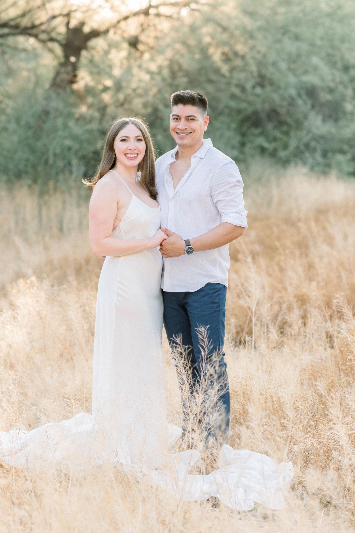 A couple poses together in a field of dried grass during sunset for an engagement photo.