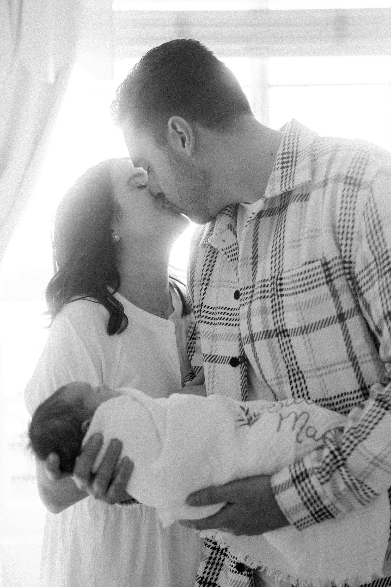 Tender black and white moment between couple gazing at their newborn baby swaddled in white.