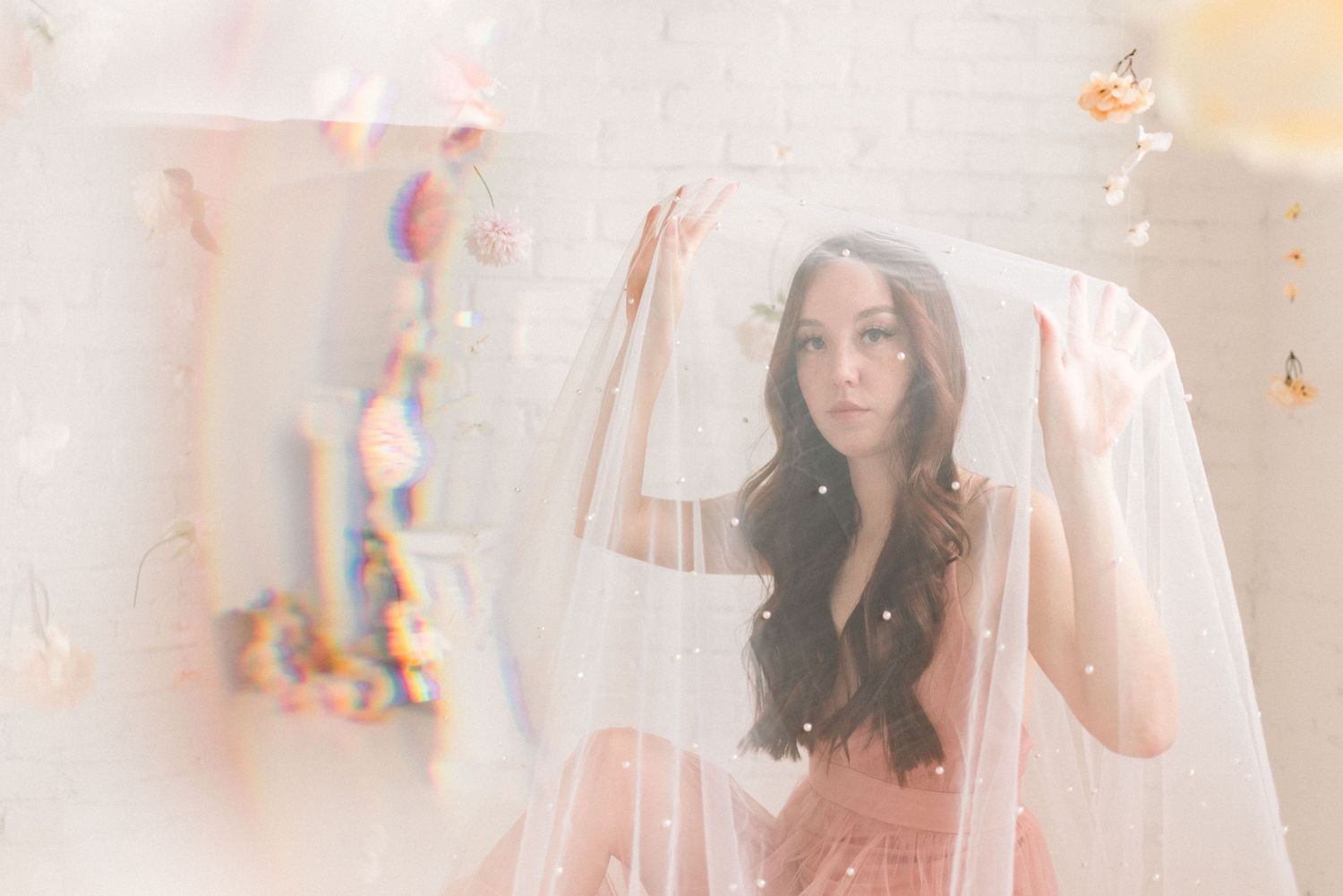 Dreamy portrait in soft pink tones with floating flowers and ethereal lighting effects.