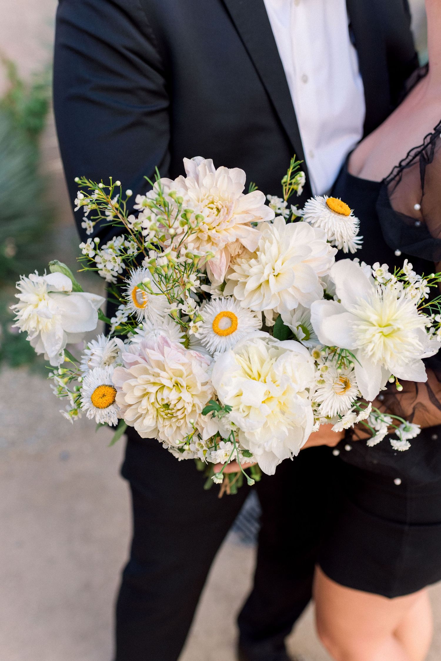 Elegant white and yellow floral bouquet with daisies held against a dark suit.