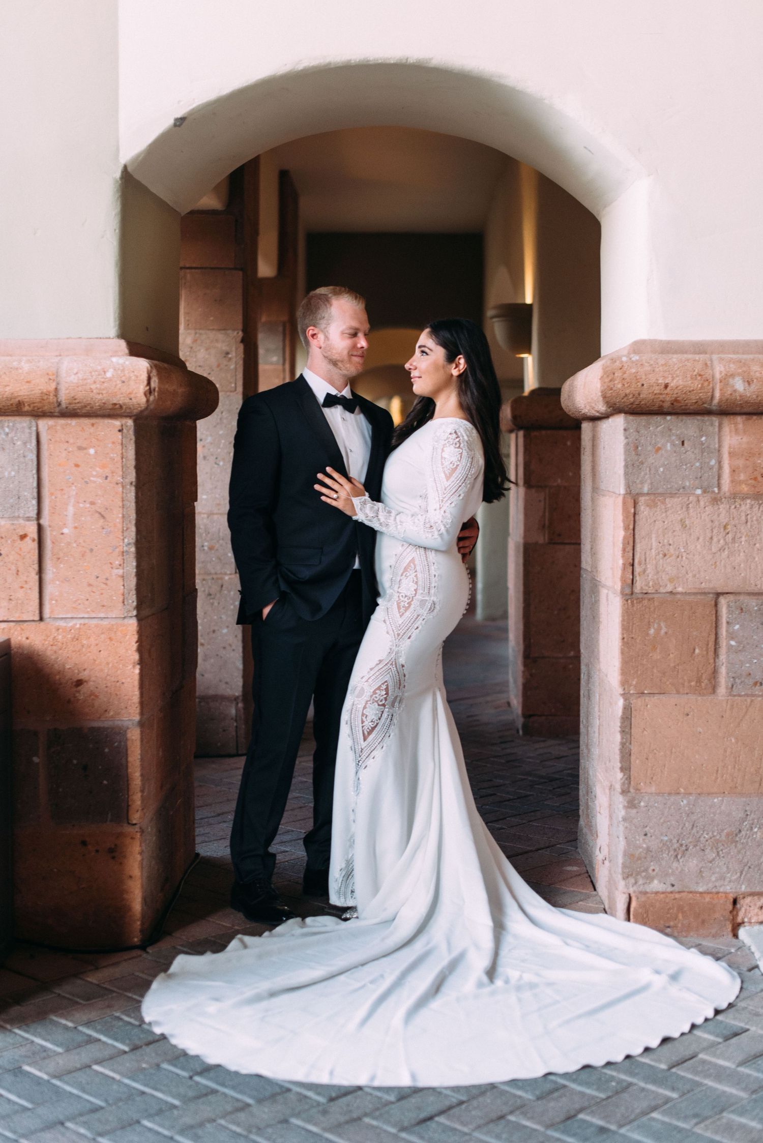 A bride and groom share an intimate moment against a stone archway backdrop.