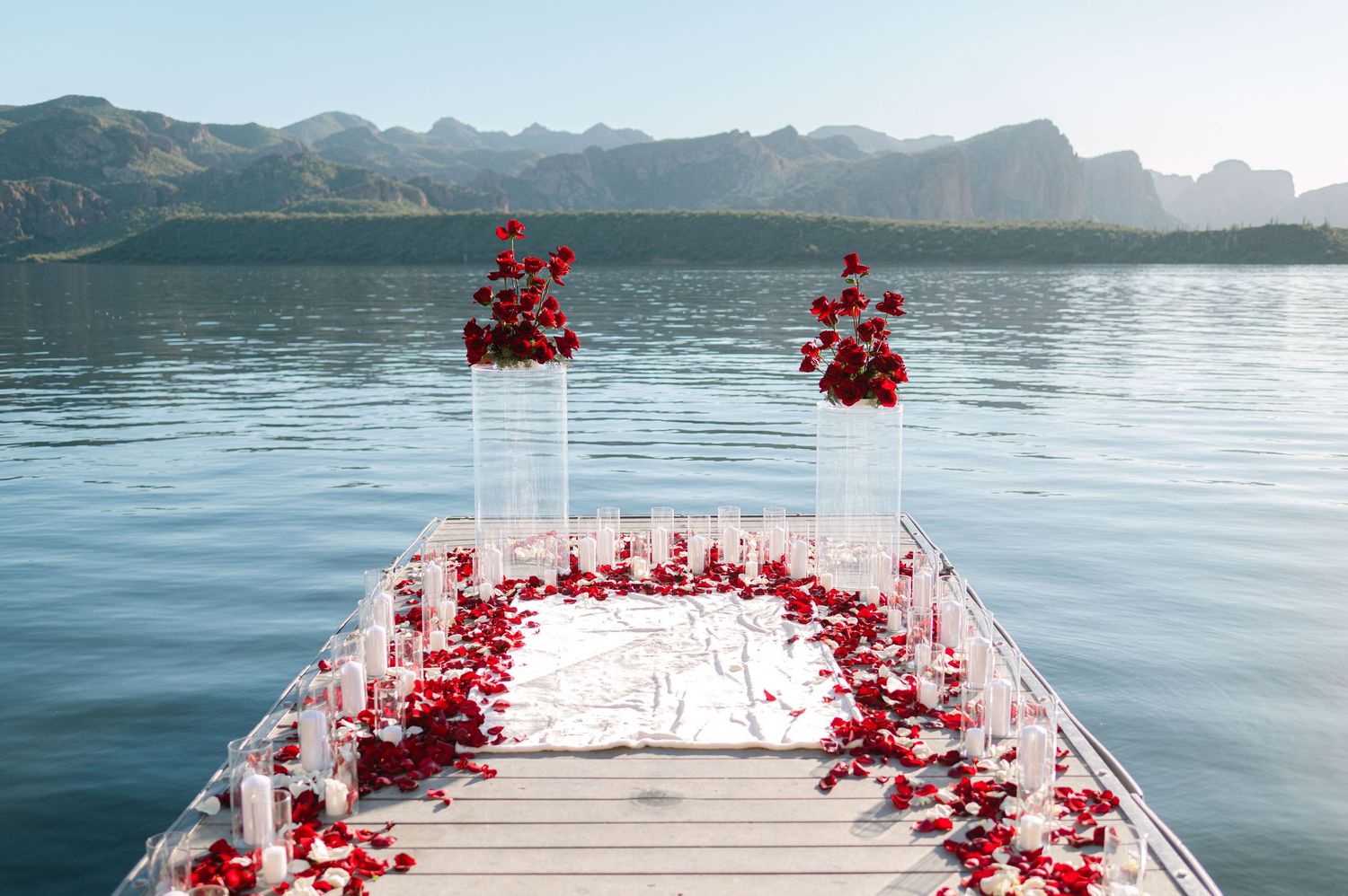 Wooden dock decorated with red rose petals leading to stunning mountain lake views.