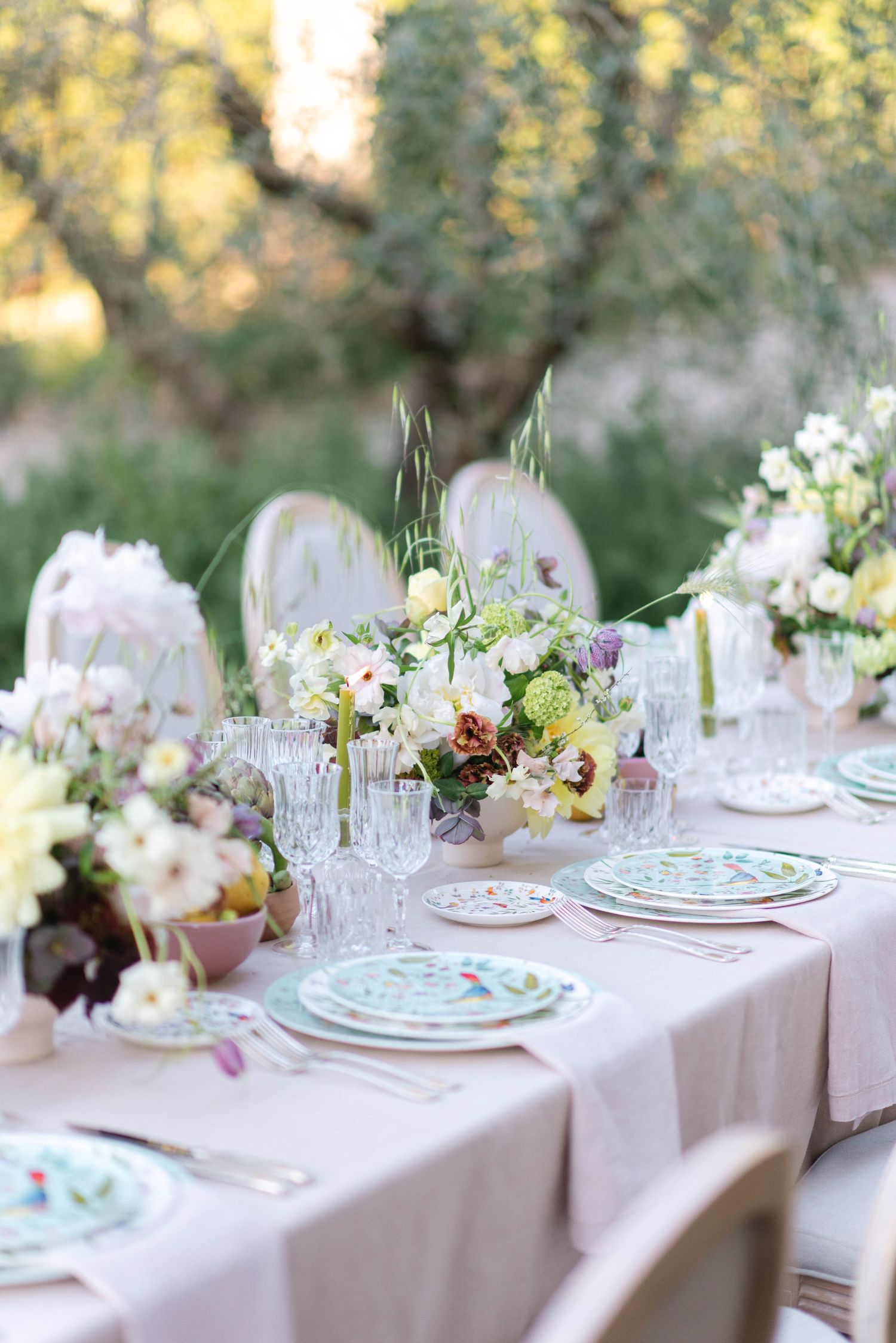 Elegant garden wedding table setting with pastel flowers and fine china on white linens.