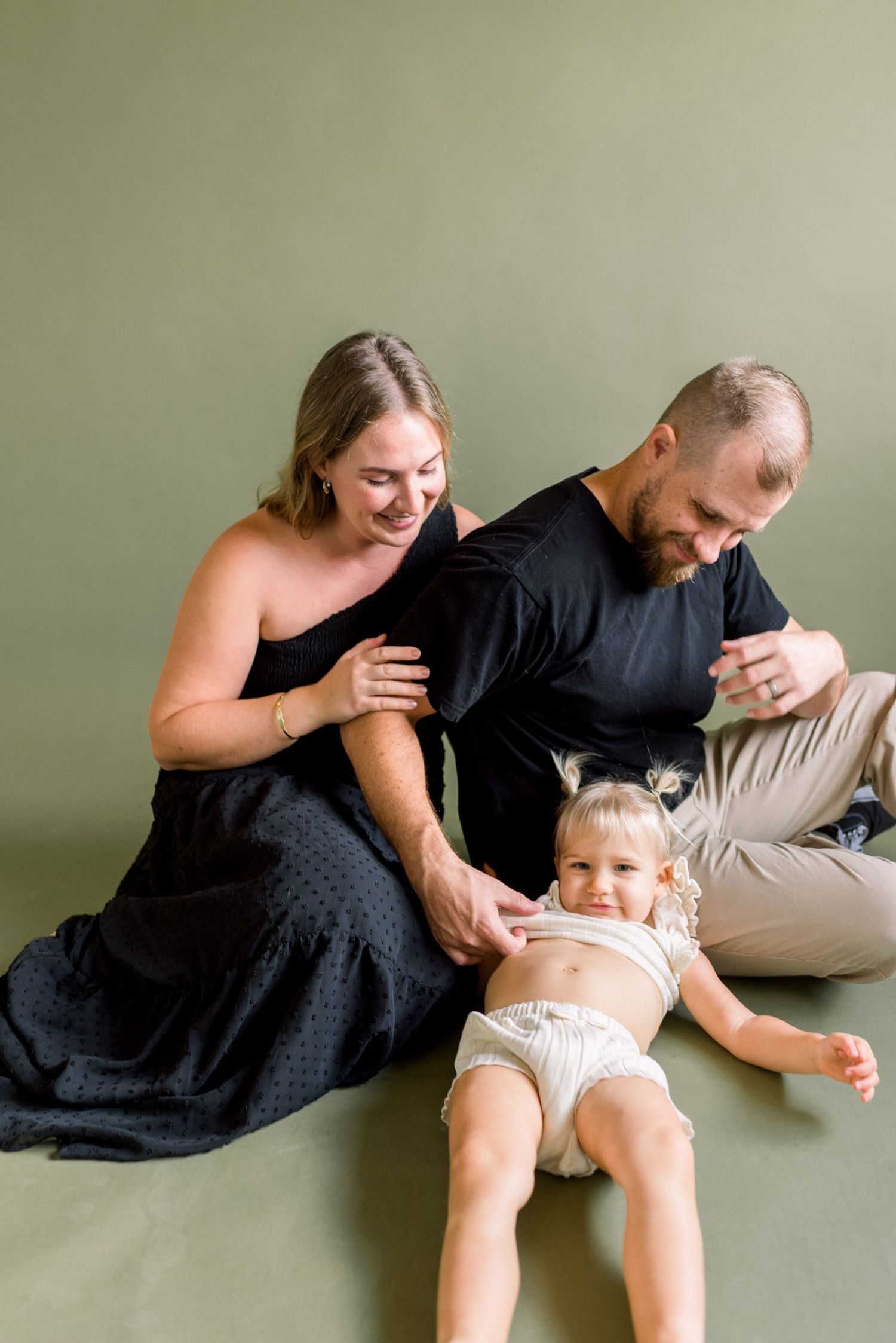 Family of three relaxing together during an intimate indoor photo session on a plain background.
