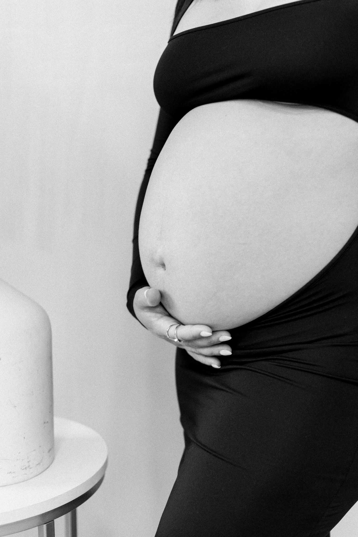 Black and white close-up of pregnant belly with hands cradling the bump.