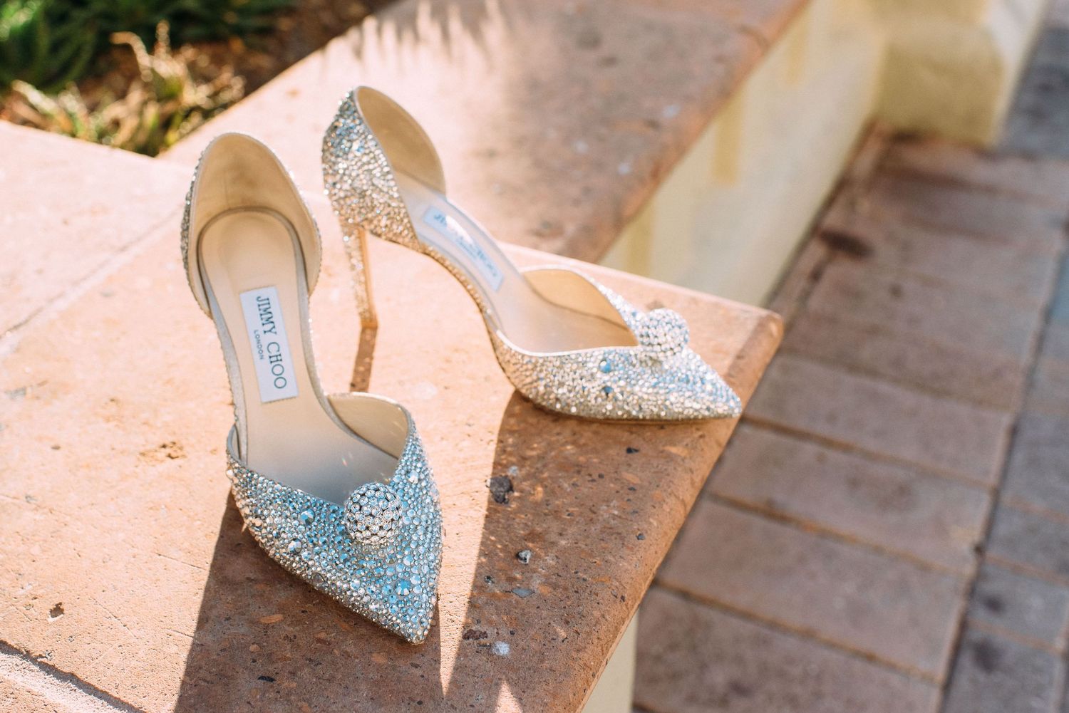 Sparkly crystal-embellished wedding shoes placed on stone ledge.