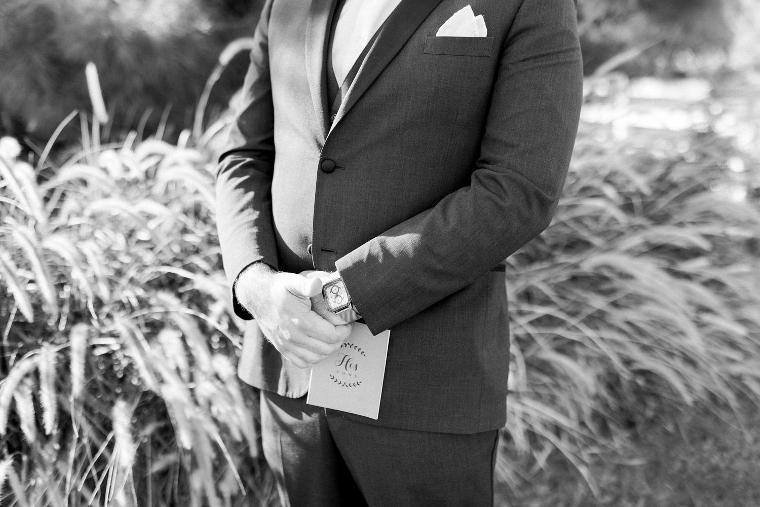 Close-up detail shot of a groom adjusting his suit jacket in black and white.
