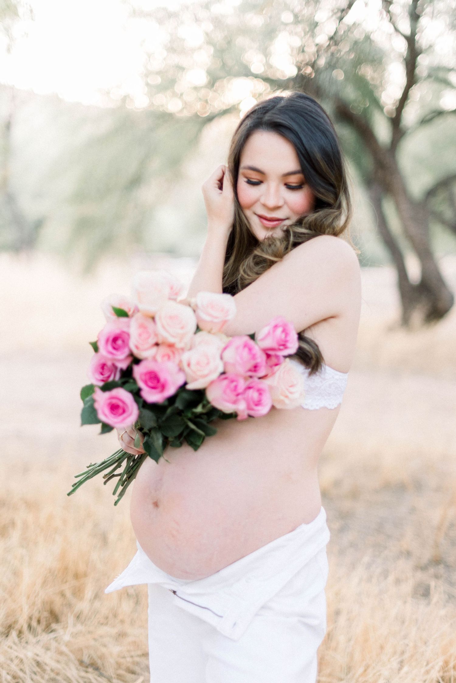 Dreamy maternity portrait with pink roses against a soft natural backdrop.