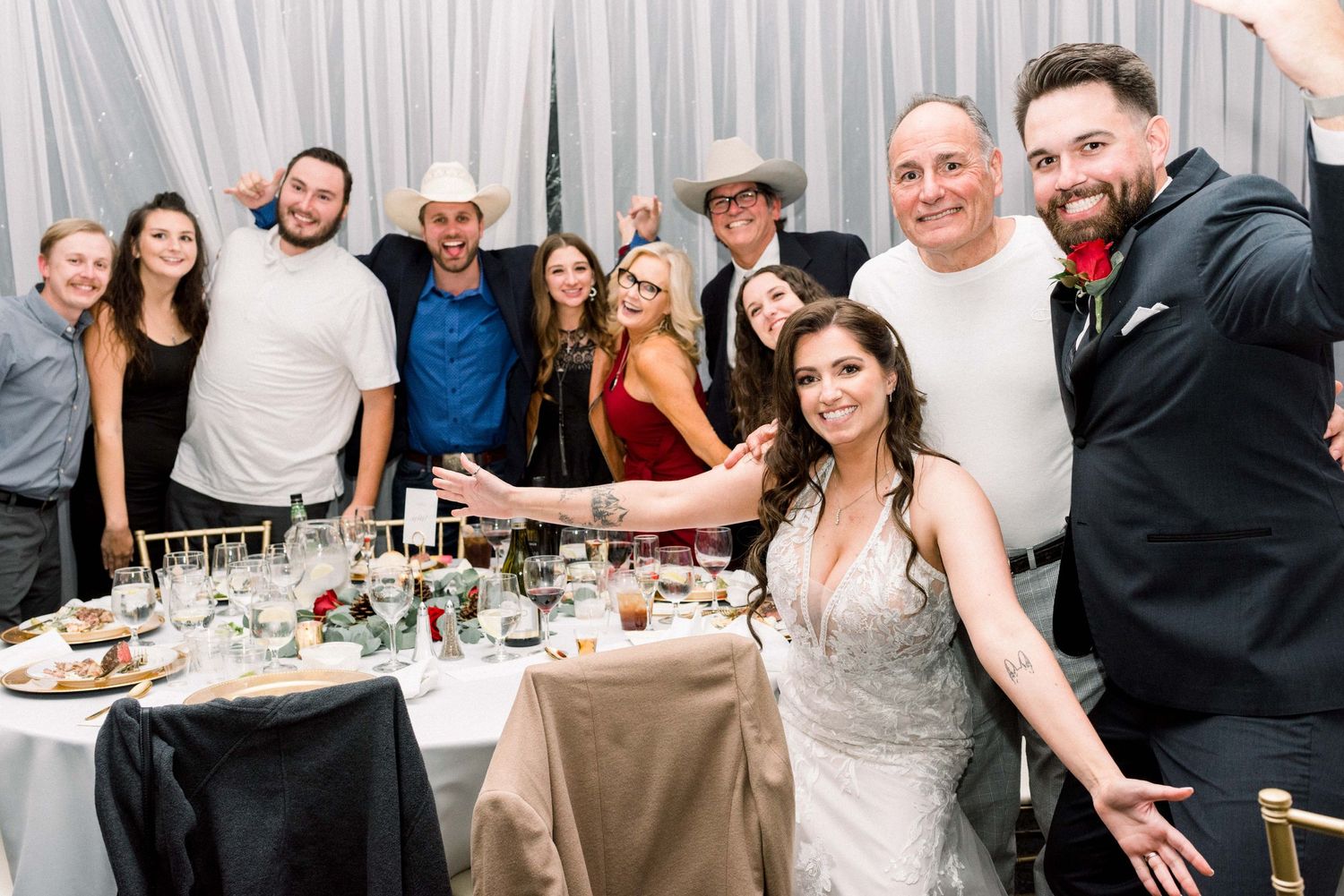 Wedding party poses together around reception table with celebratory expressions.