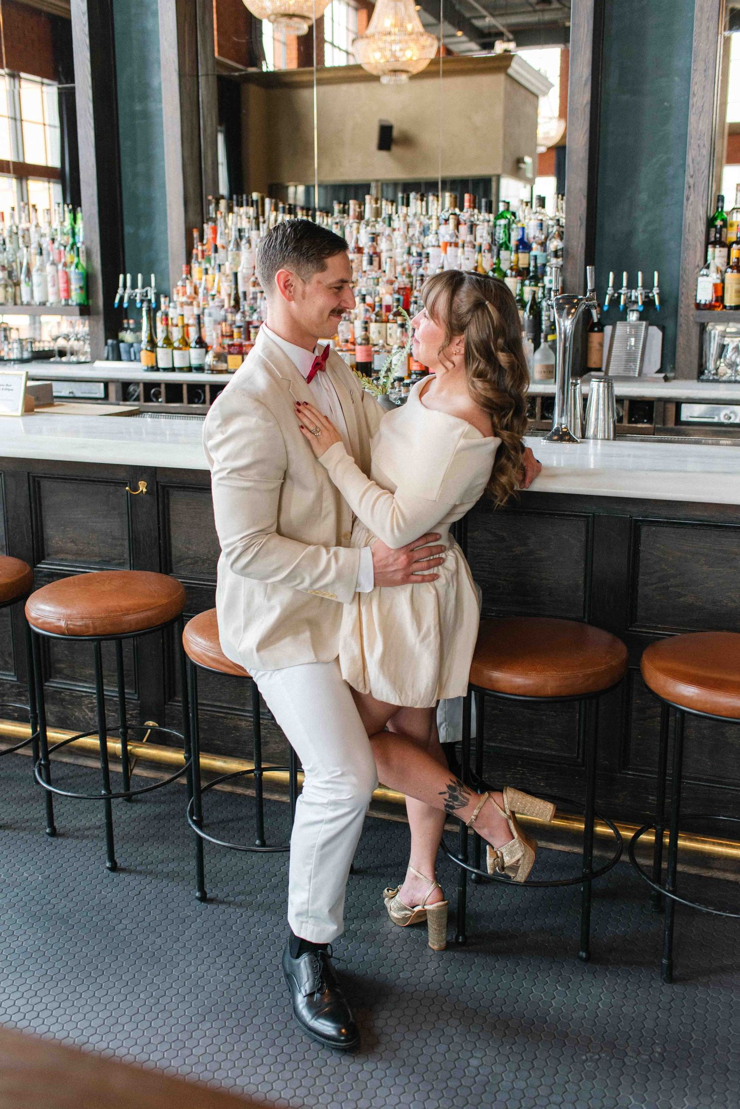 A couple in white outfits shares an intimate dance pose near a well-stocked bar counter.