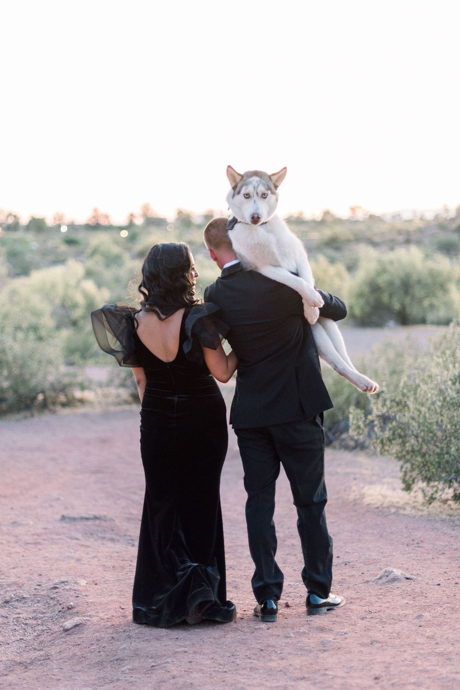 Couple walks with their husky dog on desert path during sunset photoshoot.