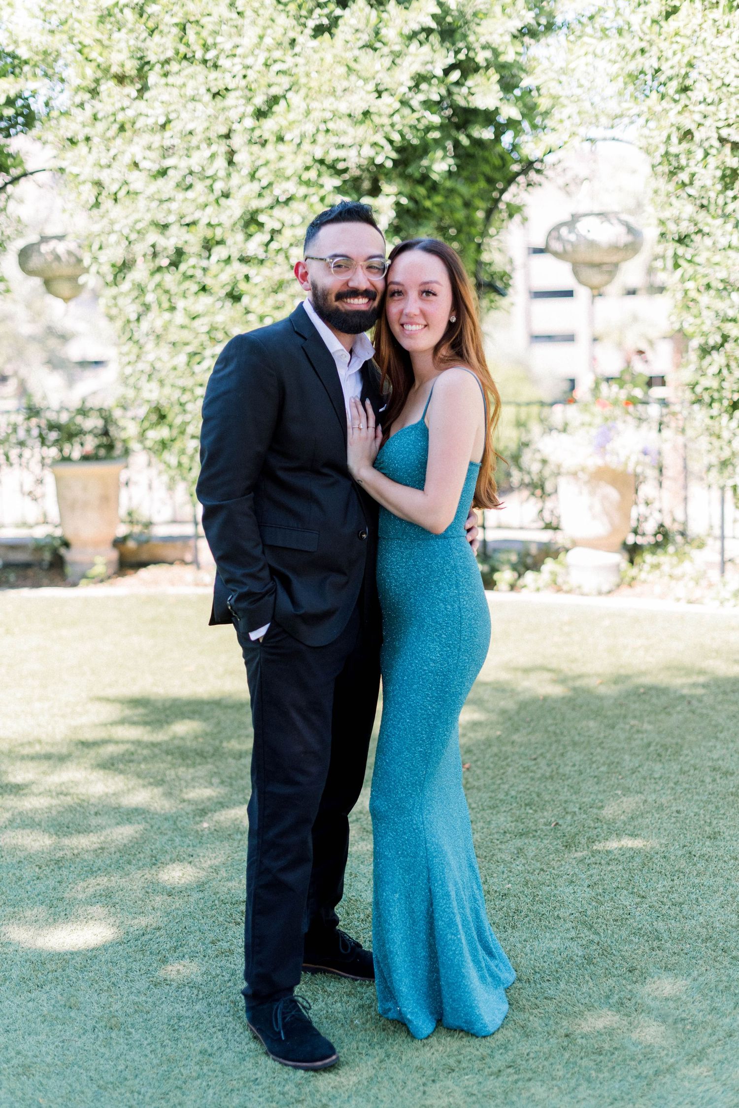 Engagement portrait of a happy couple on a sunny lawn with flowering trees.