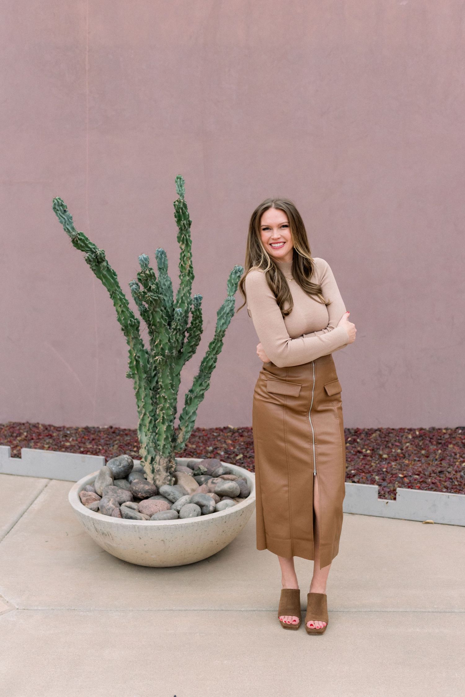 Fashion portrait with beige sweater and brown leather skirt next to desert cactus arrangement.