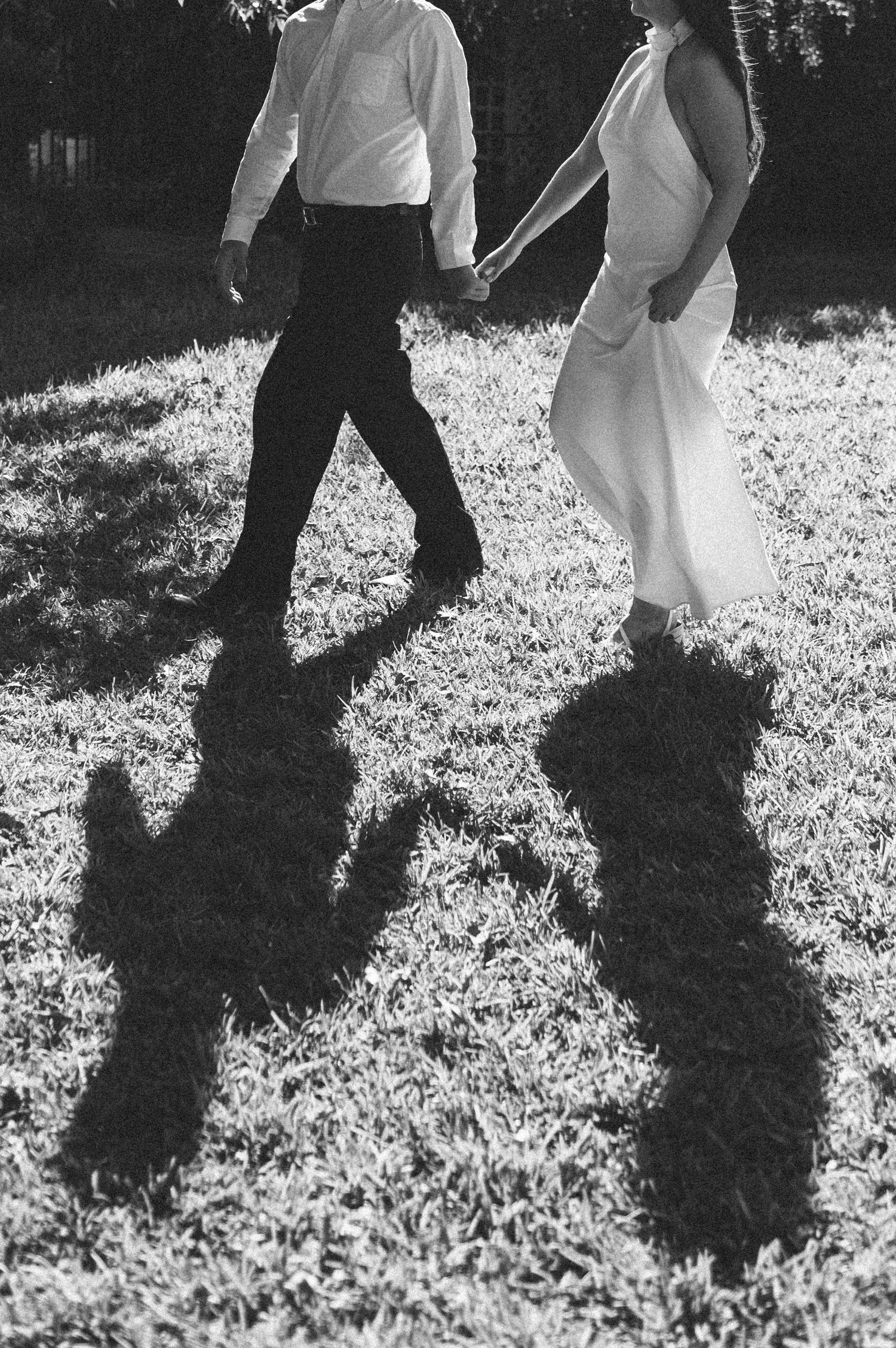 Black and white photo showing shadows of two people walking on sunlit grass.