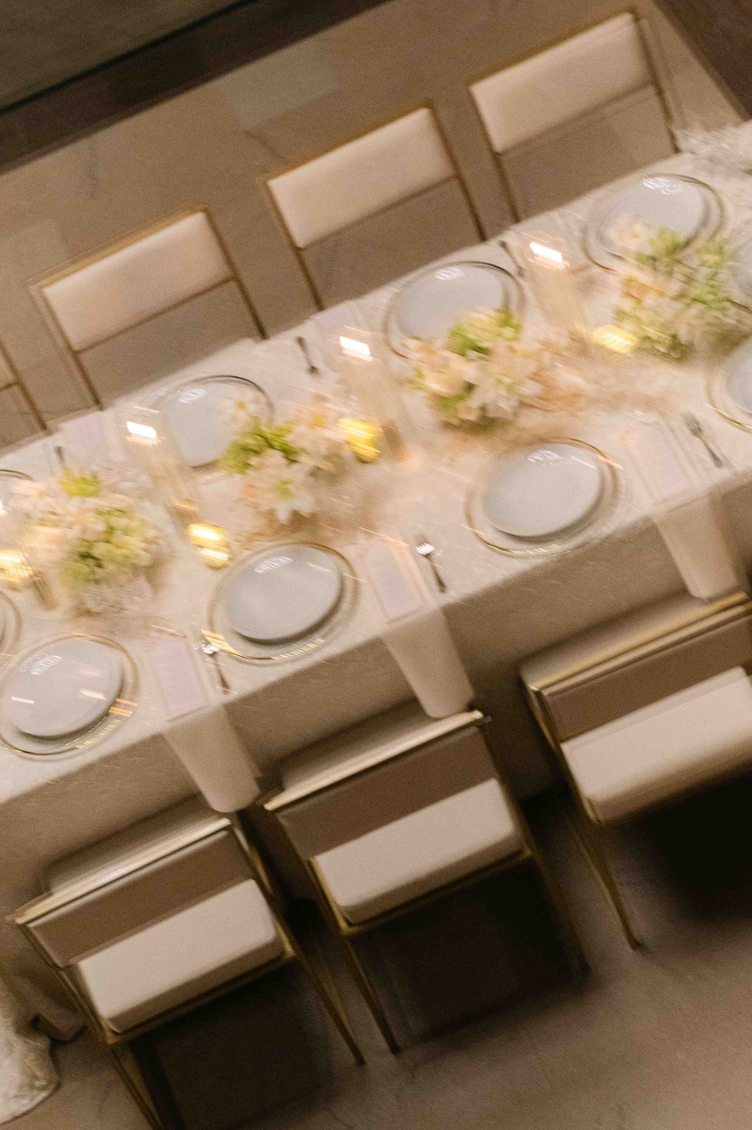 An elegant dining table set with white plates and delicate floral centerpieces illuminated by soft lighting.