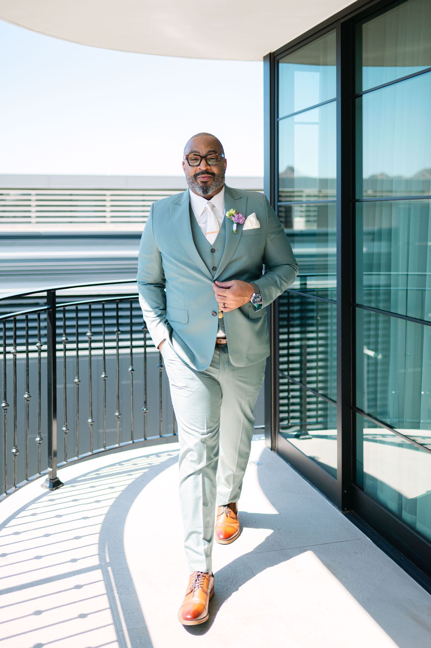 Modern balcony view showing someone in a mint green suit walking against glass windows and railing.