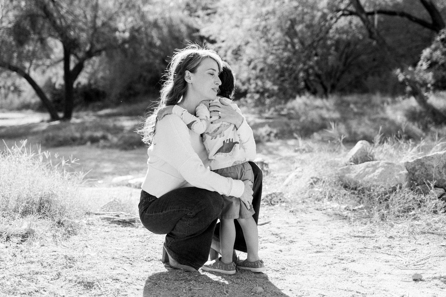 A couple sits together on a rustic dirt path surrounded by natural desert brush and vegetation.