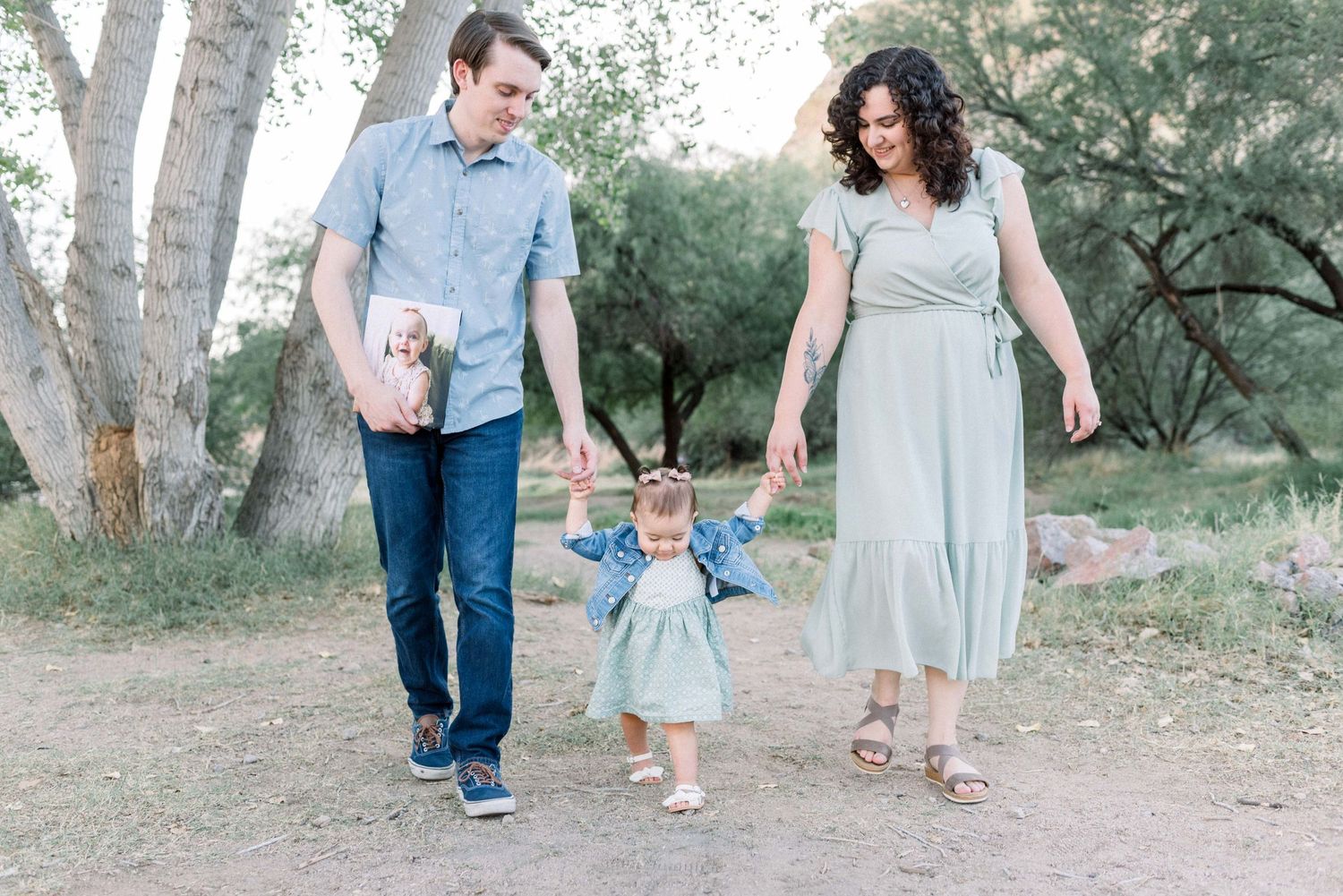 A family walks together on a dirt path through a wooded area during an outdoor photo session at sunset.