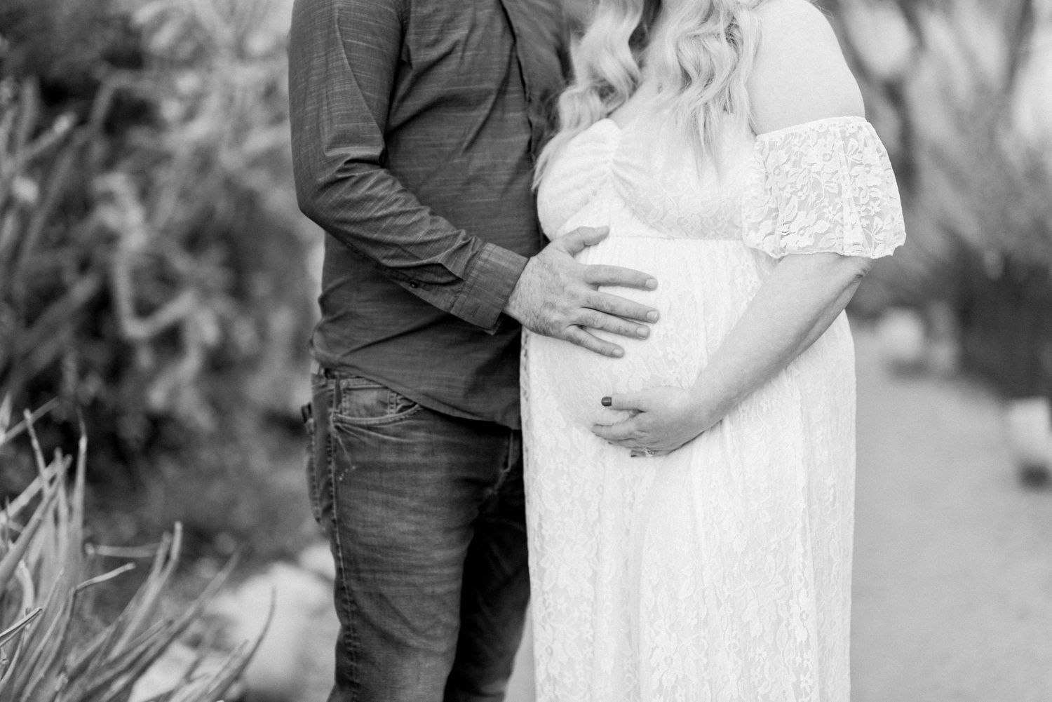 Black and white maternity photo showing couple embracing in garden setting.