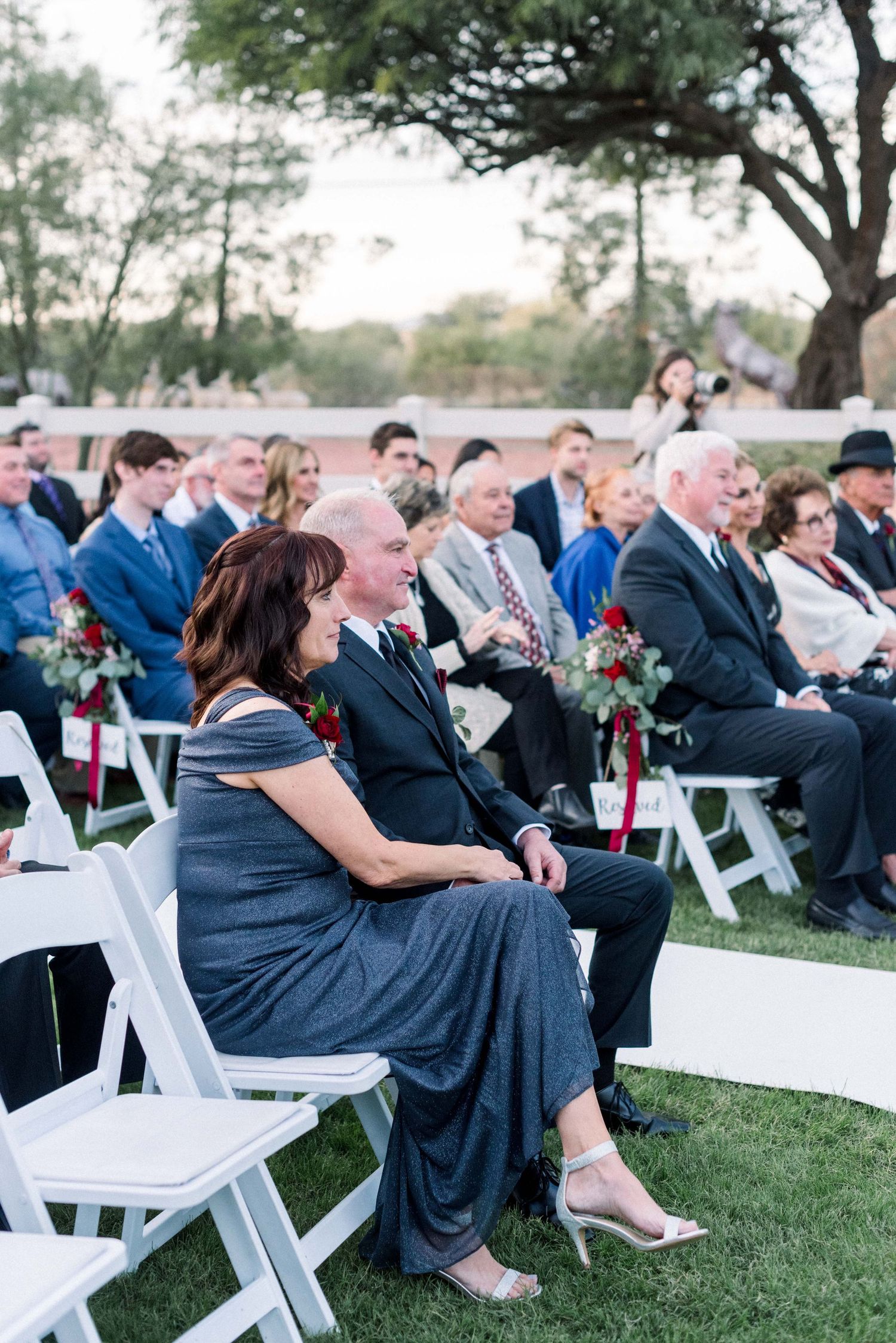 Wedding guests seated in white chairs at an outdoor ceremony venue.