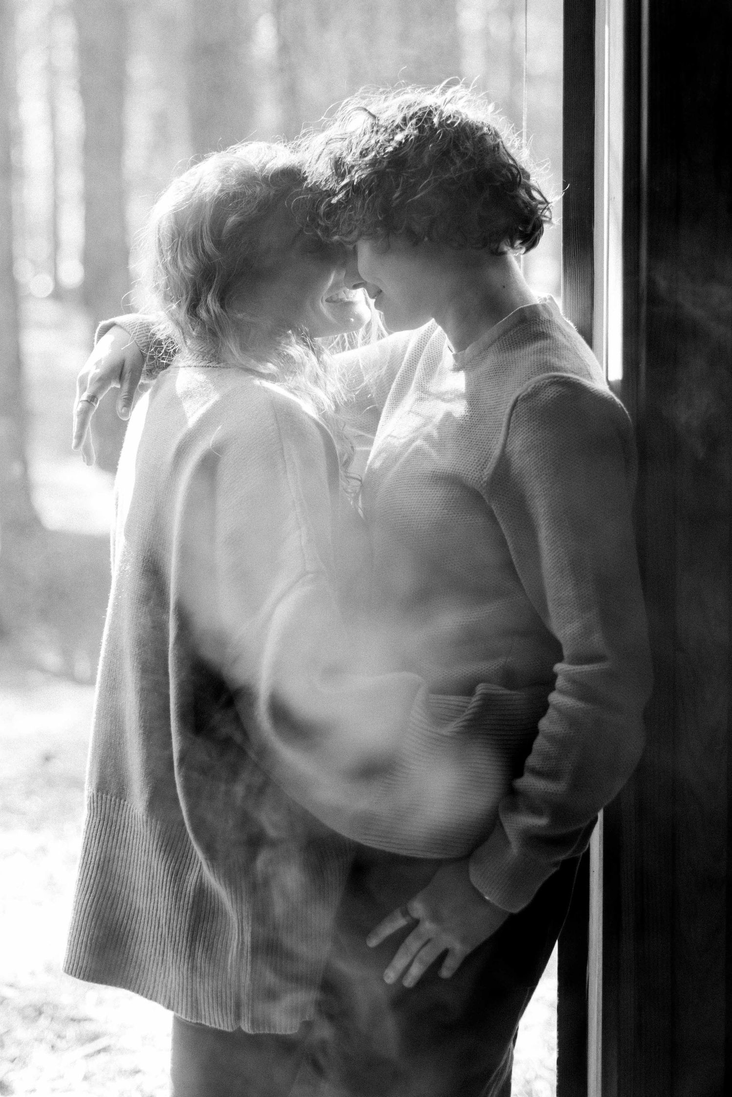 Atmospheric black and white photo of couple embracing in window light.